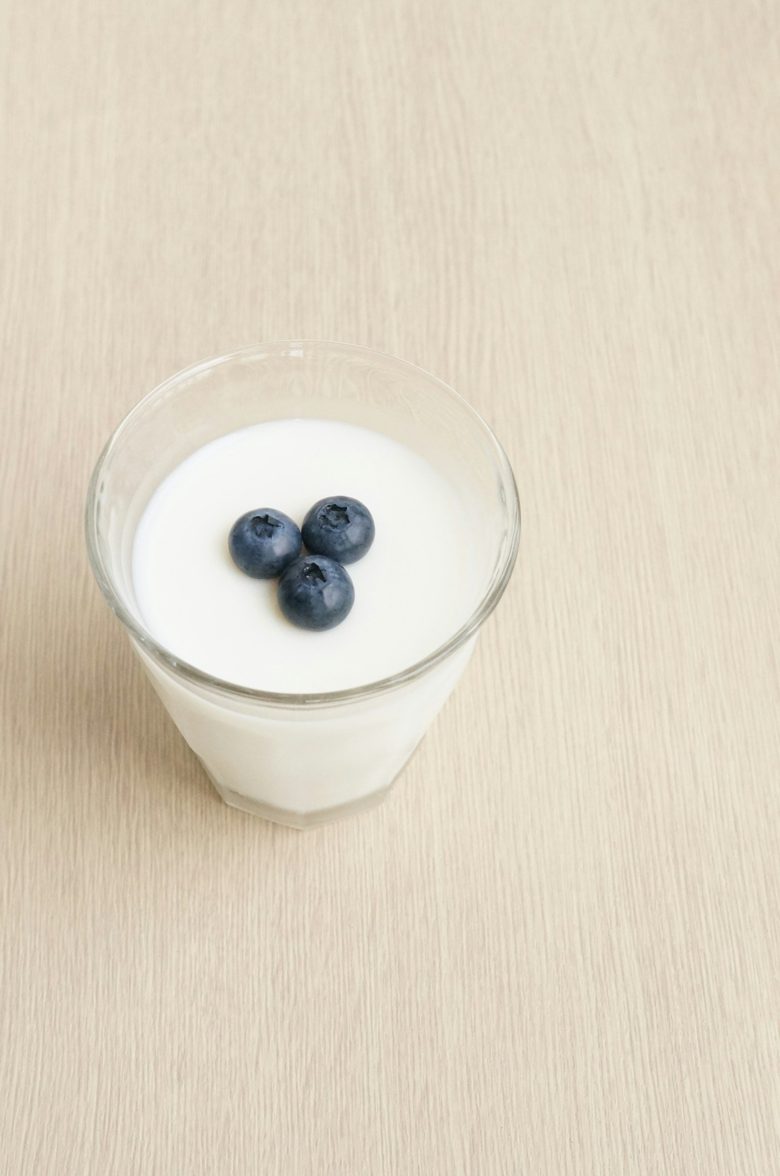 Un vaso de yogur cremoso cubierto con tres arándanos