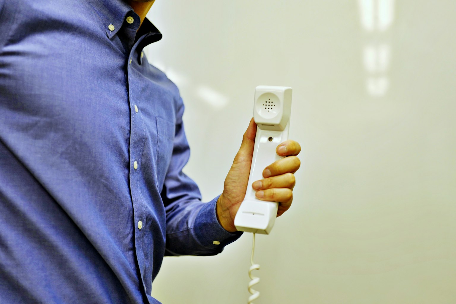 Hombre con camisa azul sosteniendo un auricular telefónico blanco