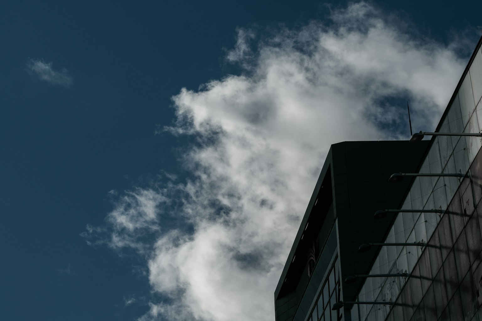 Part of a glass building against a backdrop of clouds and blue sky