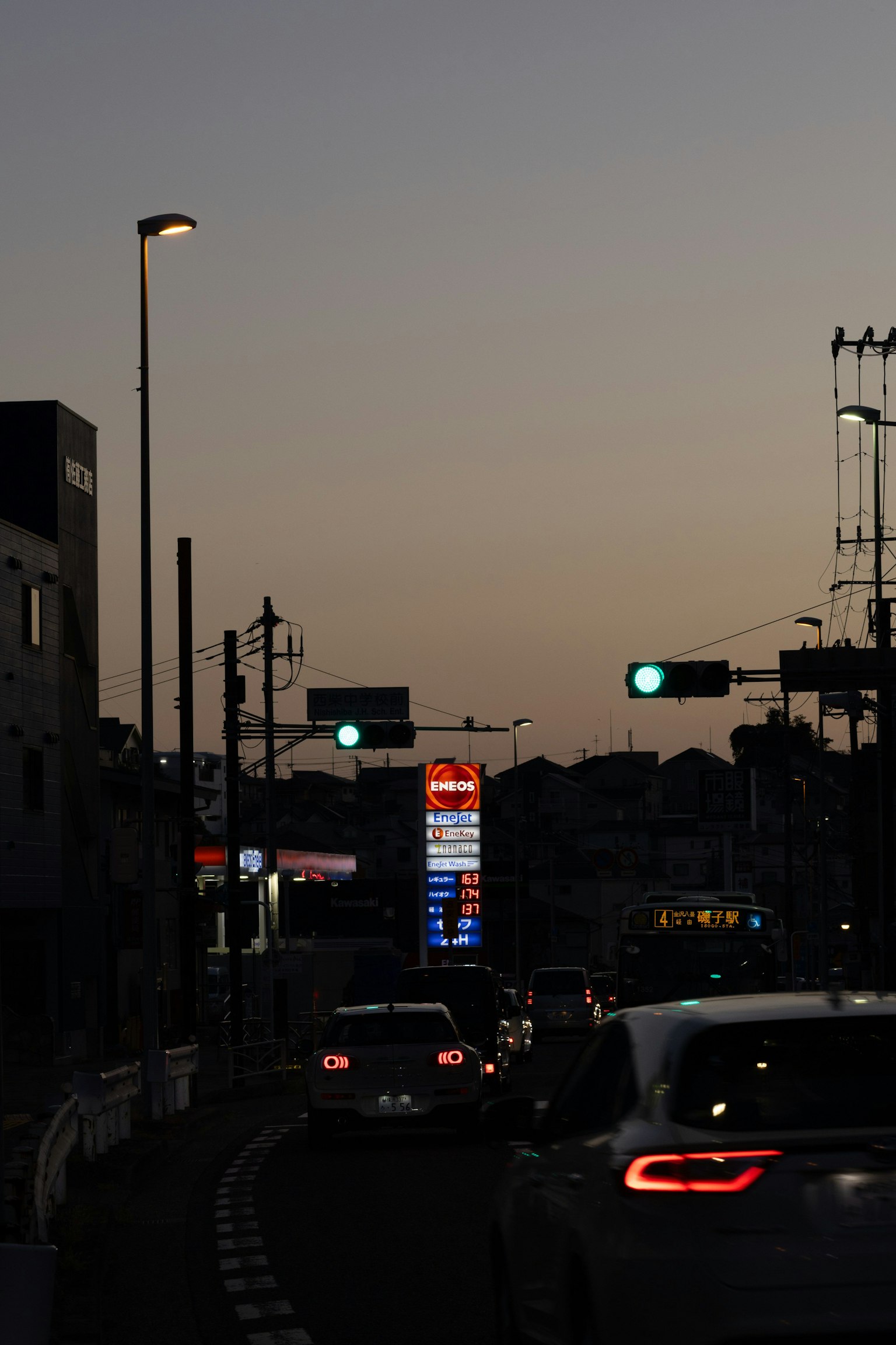 Auto su una strada al crepuscolo con semafori e un'insegna al neon