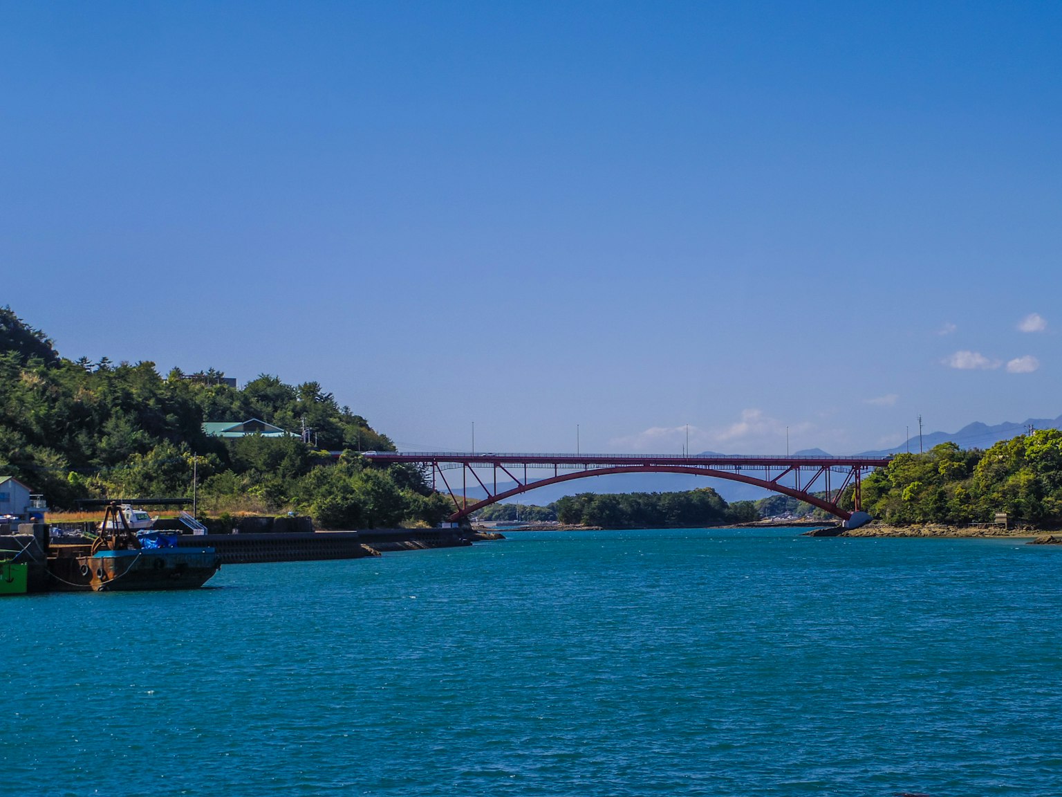 Red bridge spanning over blue waters with lush greenery around