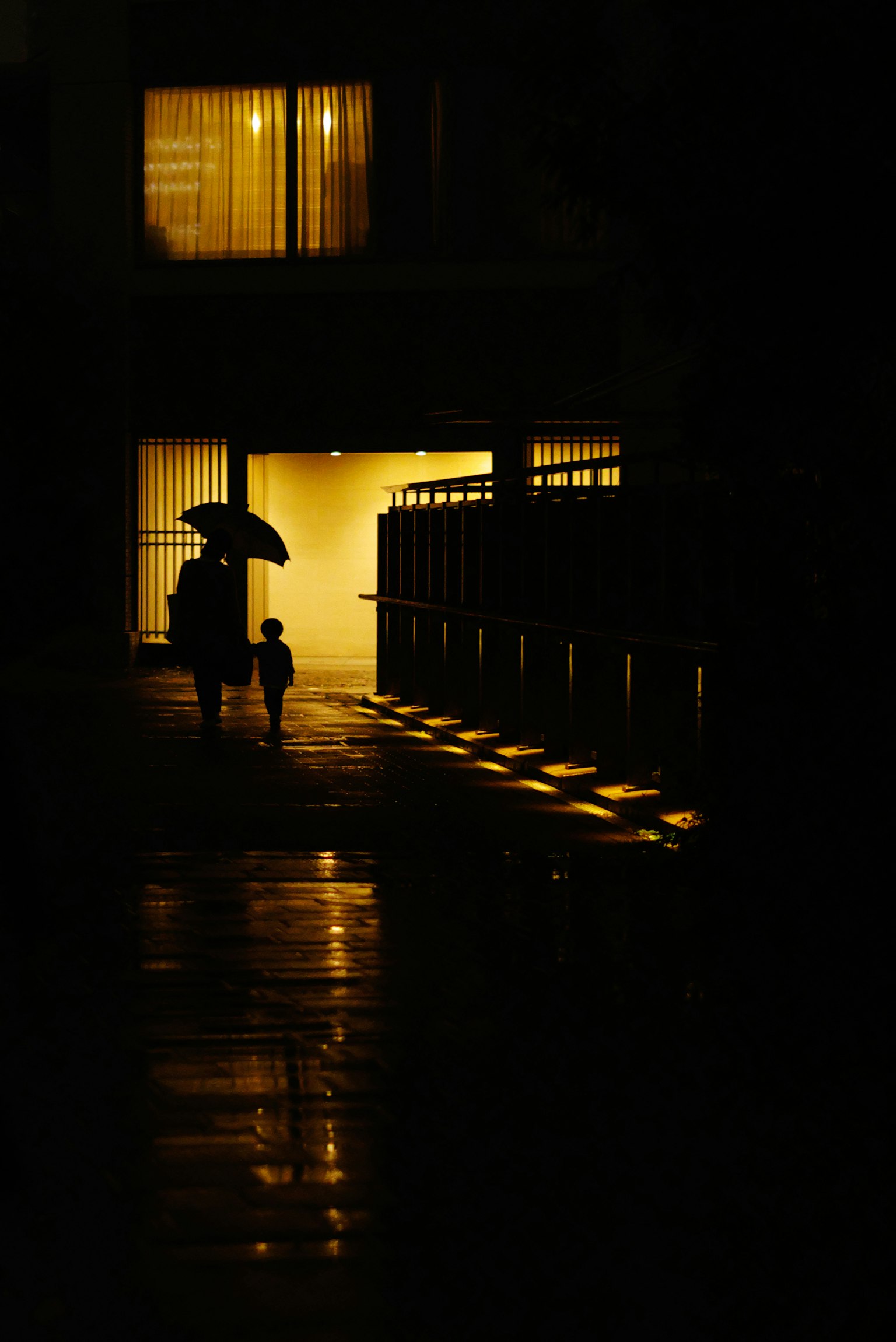 Silhouette d'un parent et d'un enfant marchant dans une rue sombre avec une lumière de fenêtre brillante