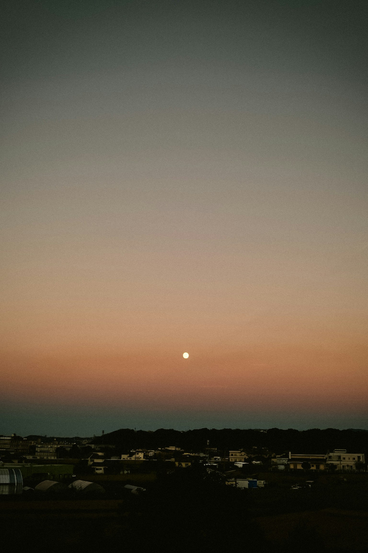 夕焼けの空に浮かぶ月と静かな街の風景