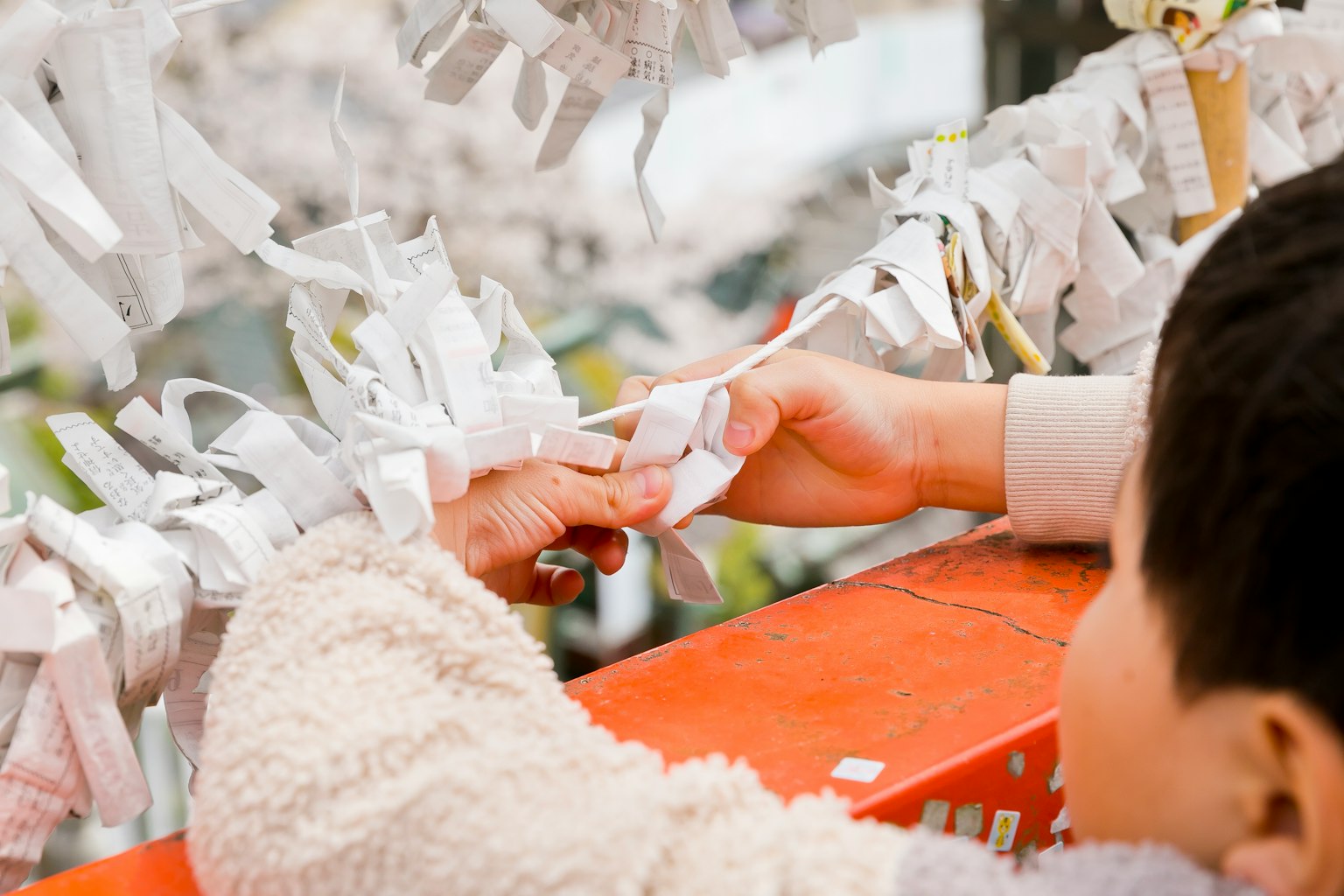 A child and an adult hand tying white paper strips together