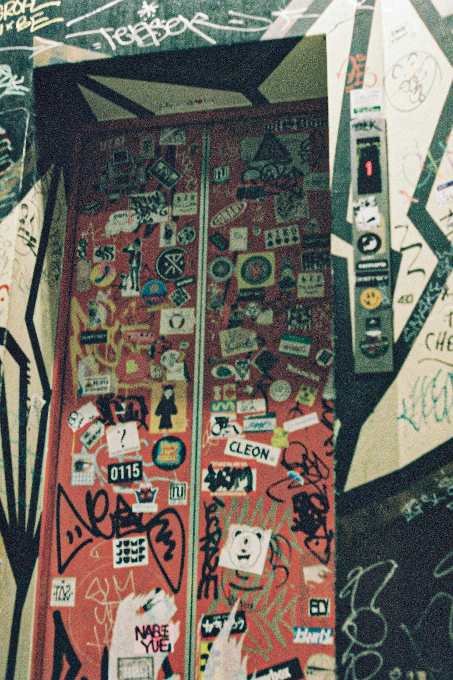 Cửa thang máy màu đỏ được phủ đầy các nhãn dán và graffiti trên một bức tường có kết cấu