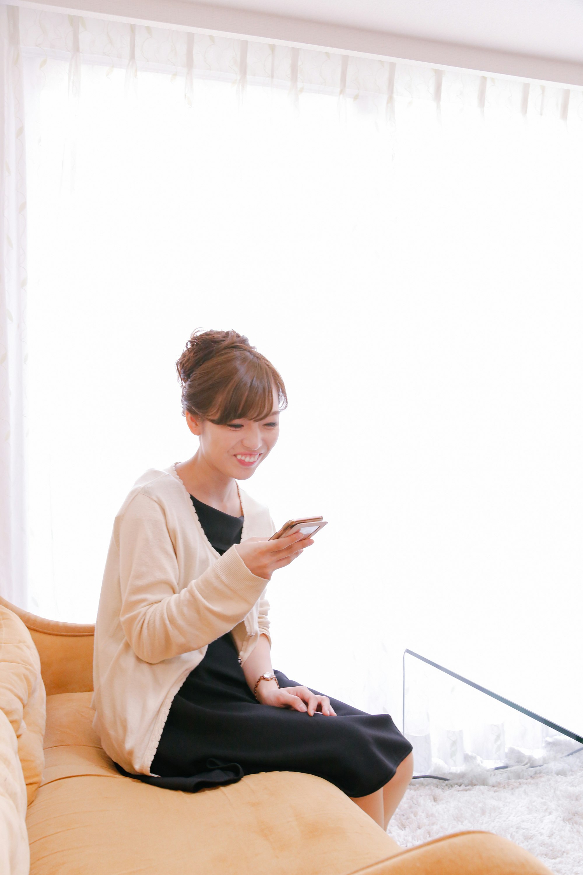 ソファに座ってスマホを見て微笑む女性のリラックスした室内シーン