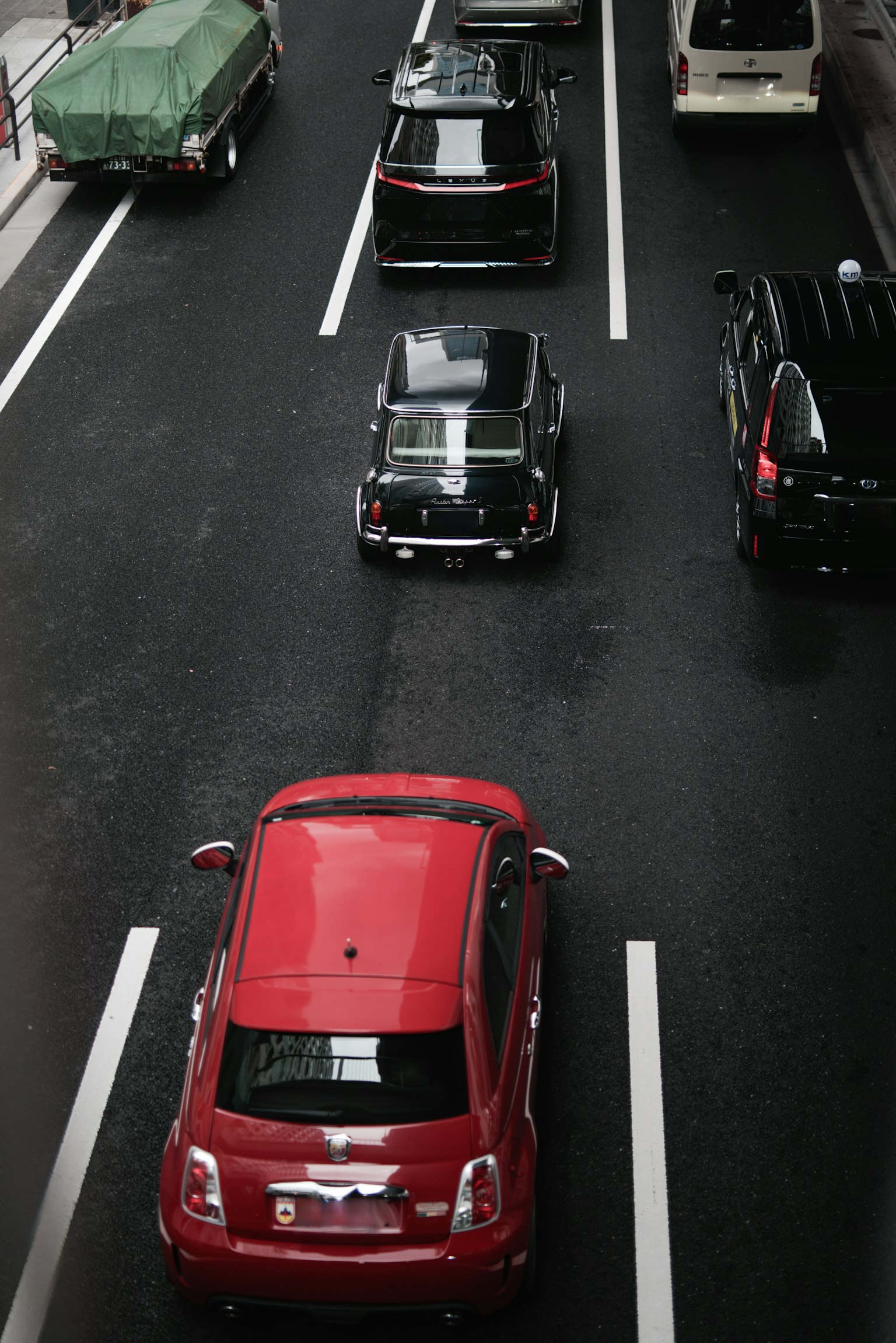 Scene of a city road with a red car in focus and several other vehicles
