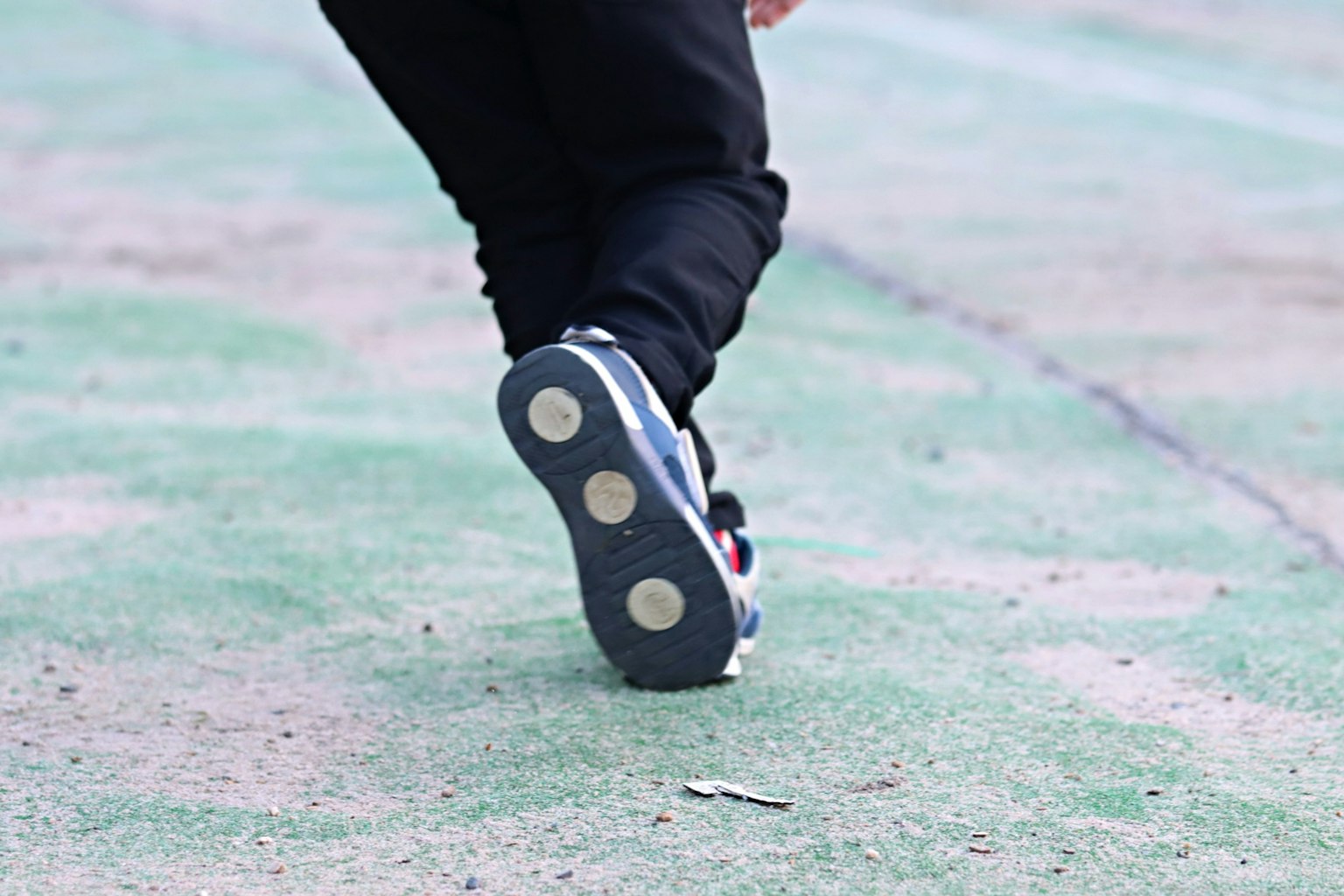 Primo piano della suola di una scarpa indossata da una persona in pantaloni neri che cammina su un terreno verde