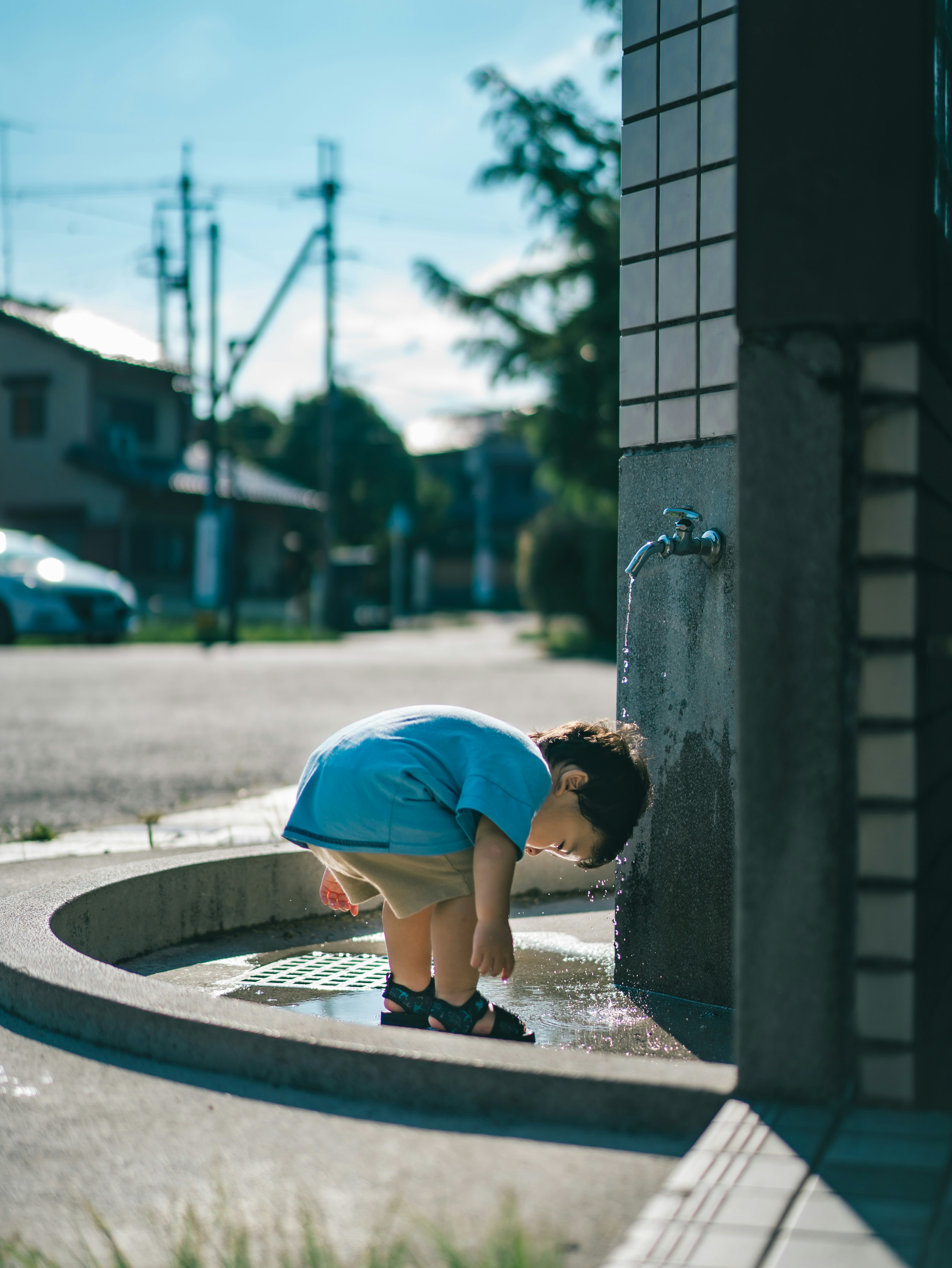頭を濡らしながら腰が引けた長男が水たまりの縁でしゃがむ路地の風景