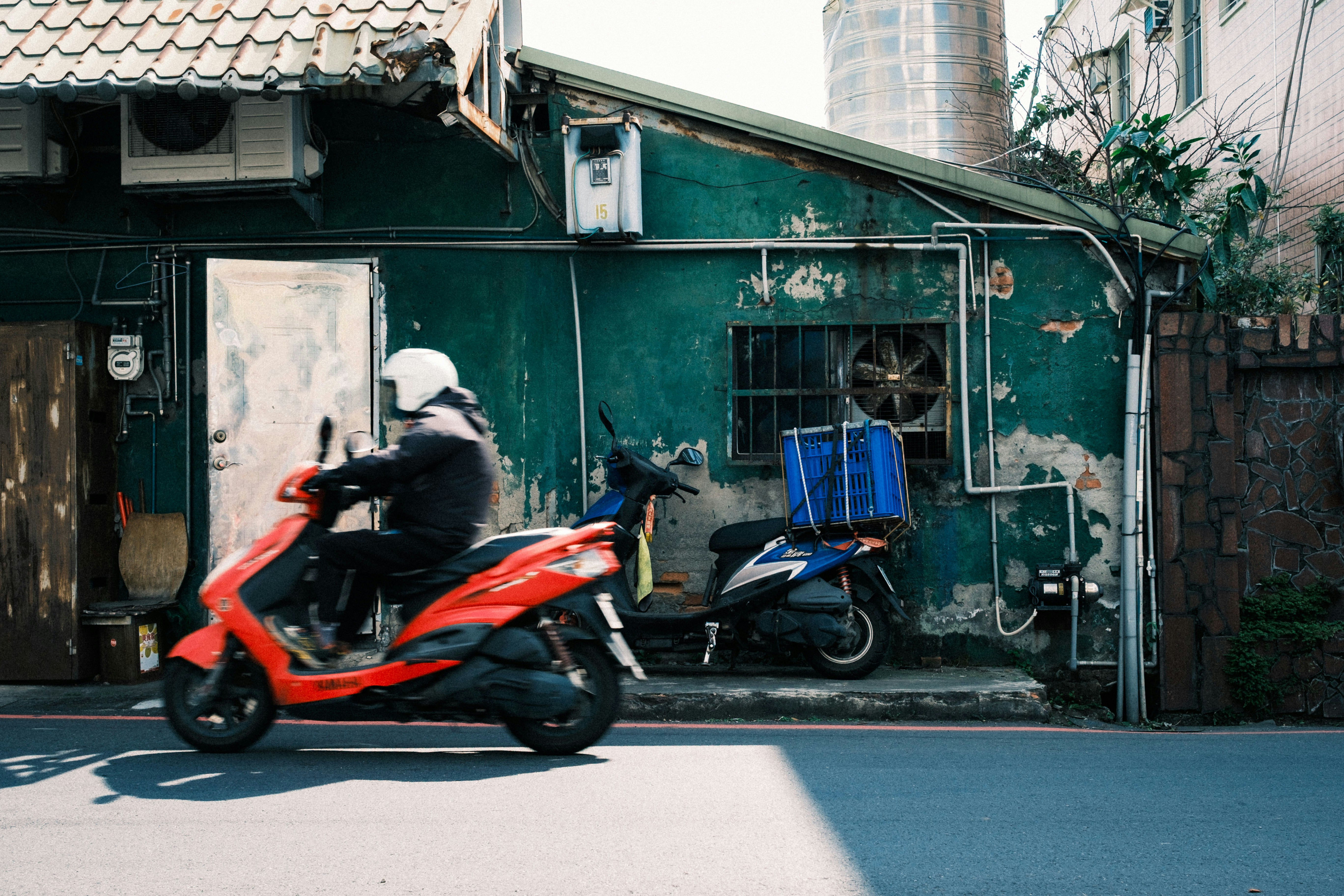 路地を走る赤いスクーターとバイクのある街角