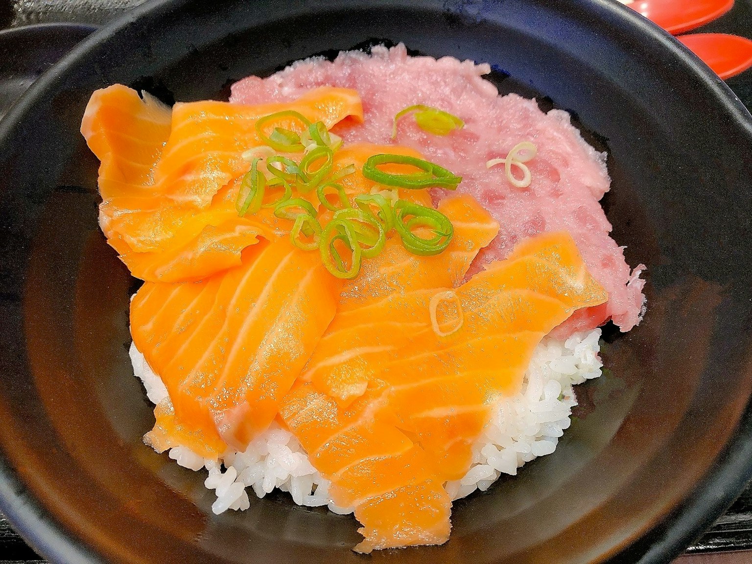 Donburi di salmone e tonno con salmone e tonno affettati su riso bianco guarnito con cipollotti