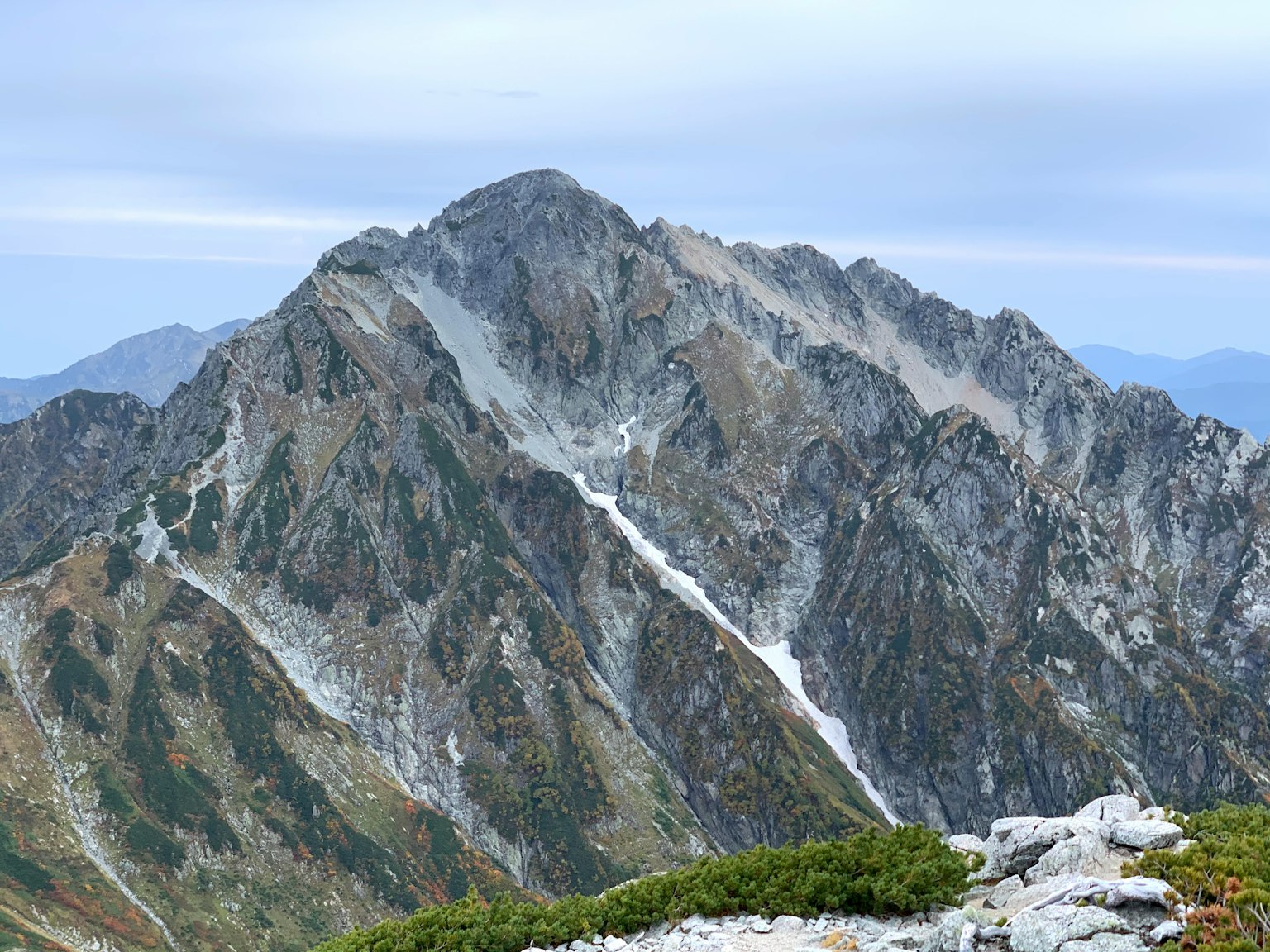 Un paysage de montagne élevé avec des pentes rocheuses et des buissons verts visibles