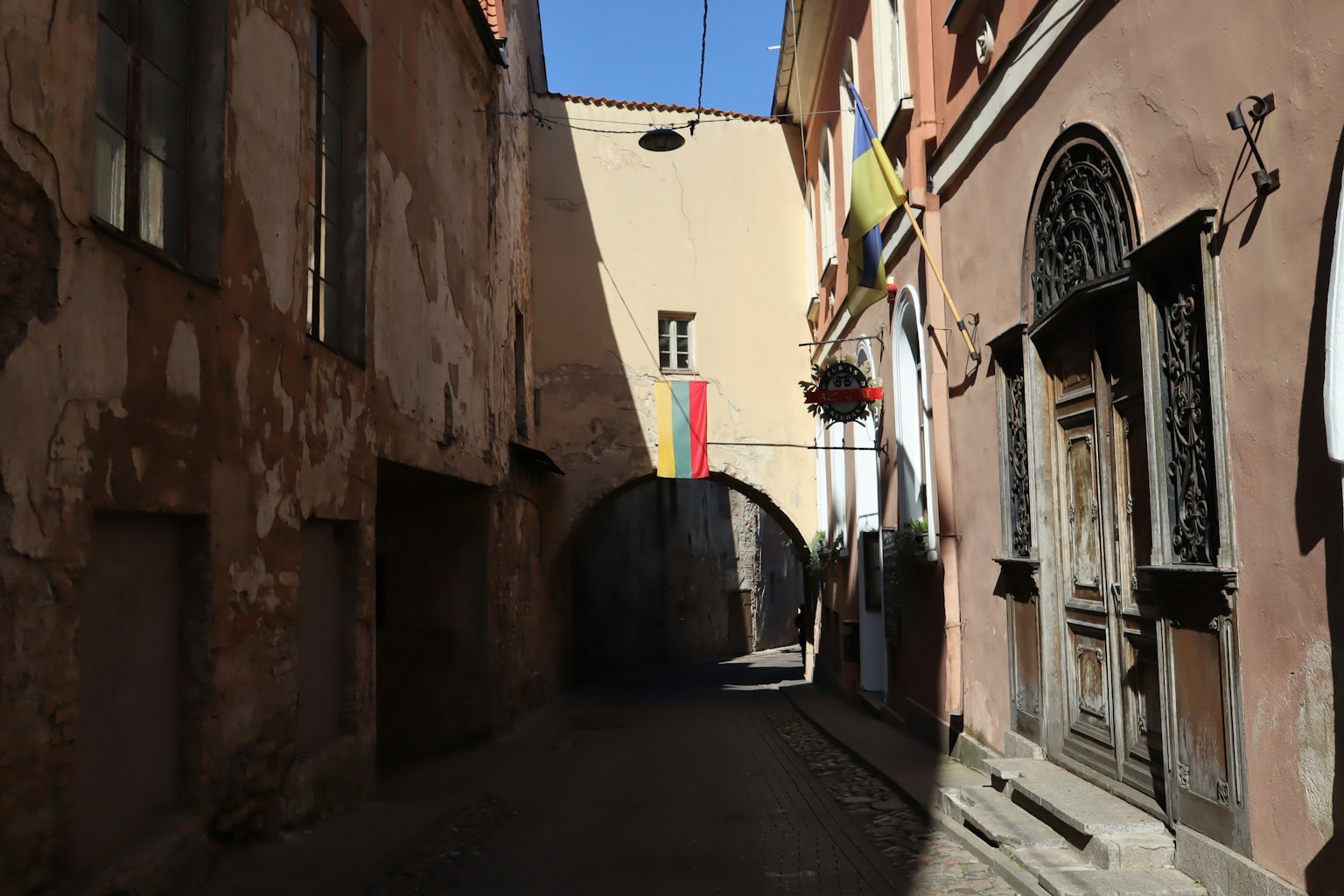 Callejón estrecho con edificios antiguos y un arco adornado con una bandera colorida