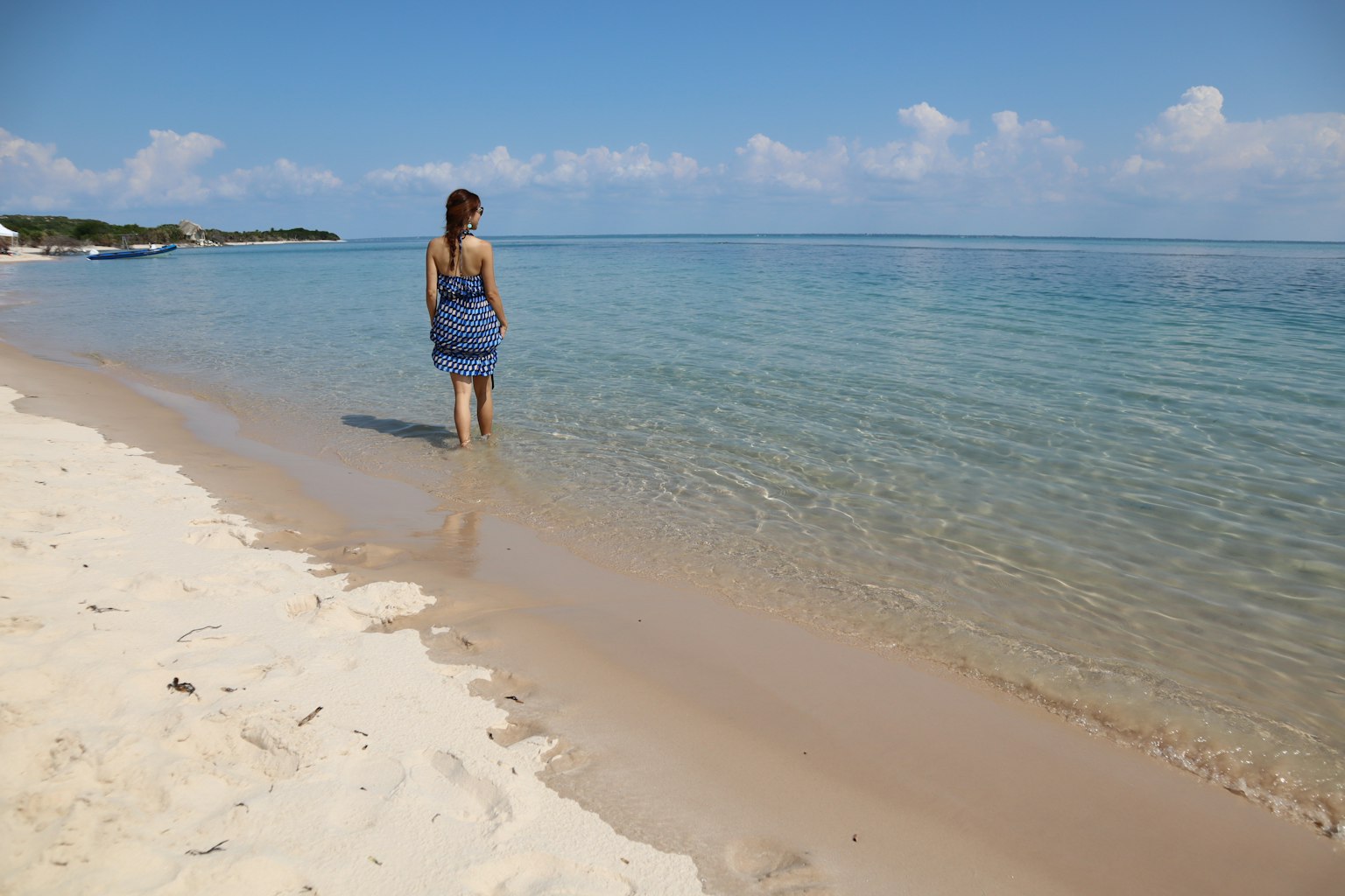 Woman wading in clear blue water on a sandy beach under a bright sky