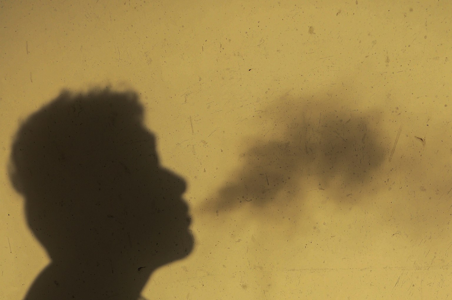 Silueta de una persona exhalando humo sobre un fondo amarillo