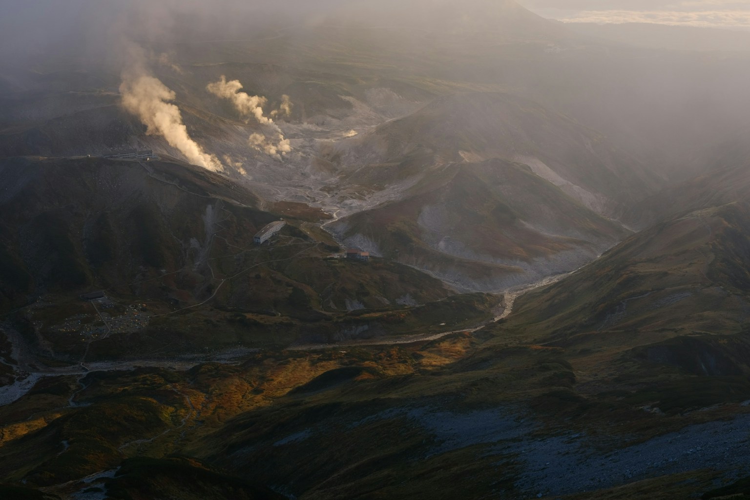 Aerial view of mountainous terrain with steam rising from geothermal hot springs