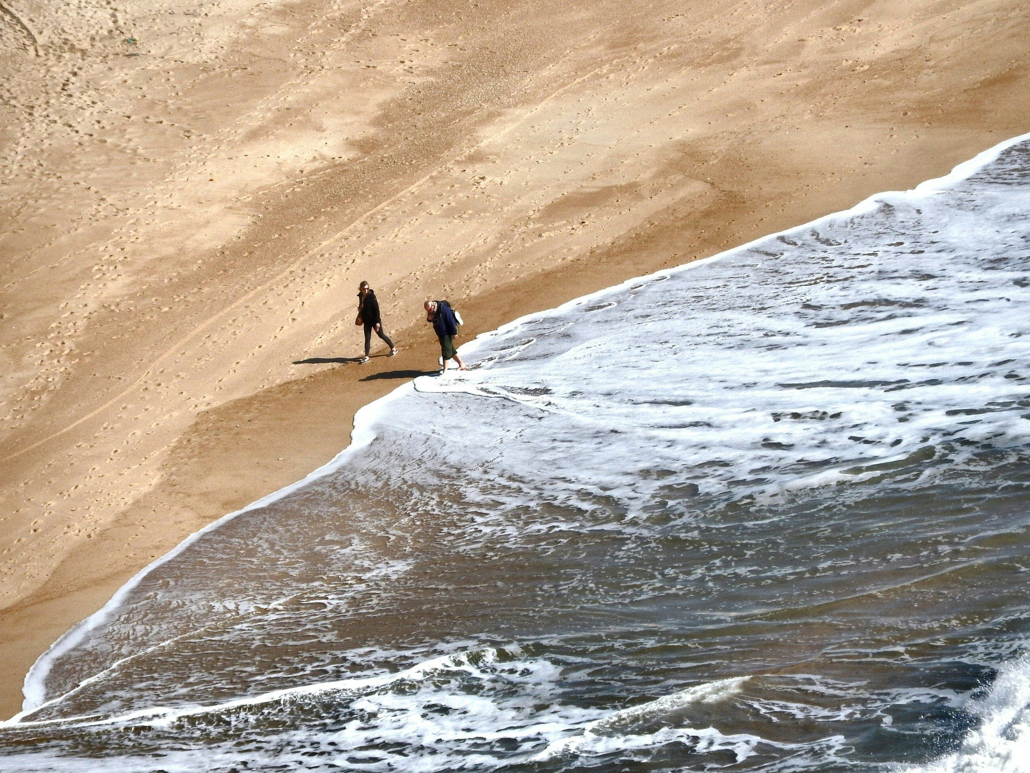 砂浜を歩く人と波打ち際の海の風景