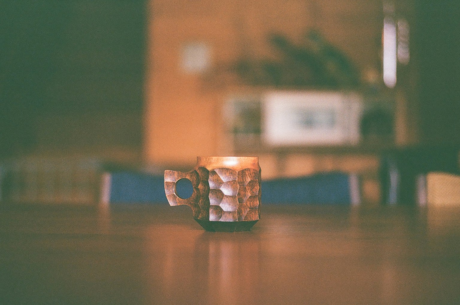 Una candela in una tazza texturizzata su un tavolo di legno con uno sfondo sfocato di cucina