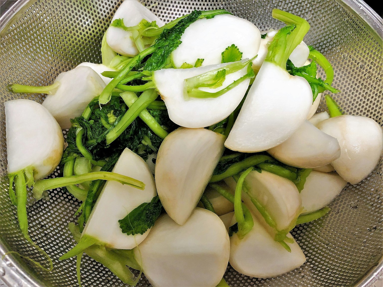 Légumes racines blancs et feuilles vertes disposés dans une passoire
