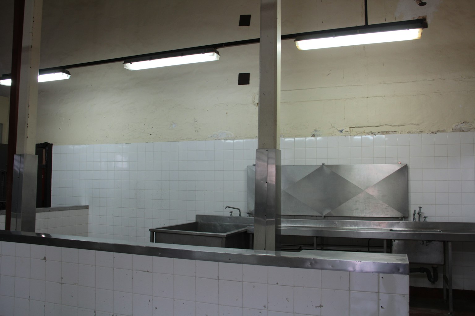 Interior of a clean kitchen featuring stainless steel worktables and white tiled walls