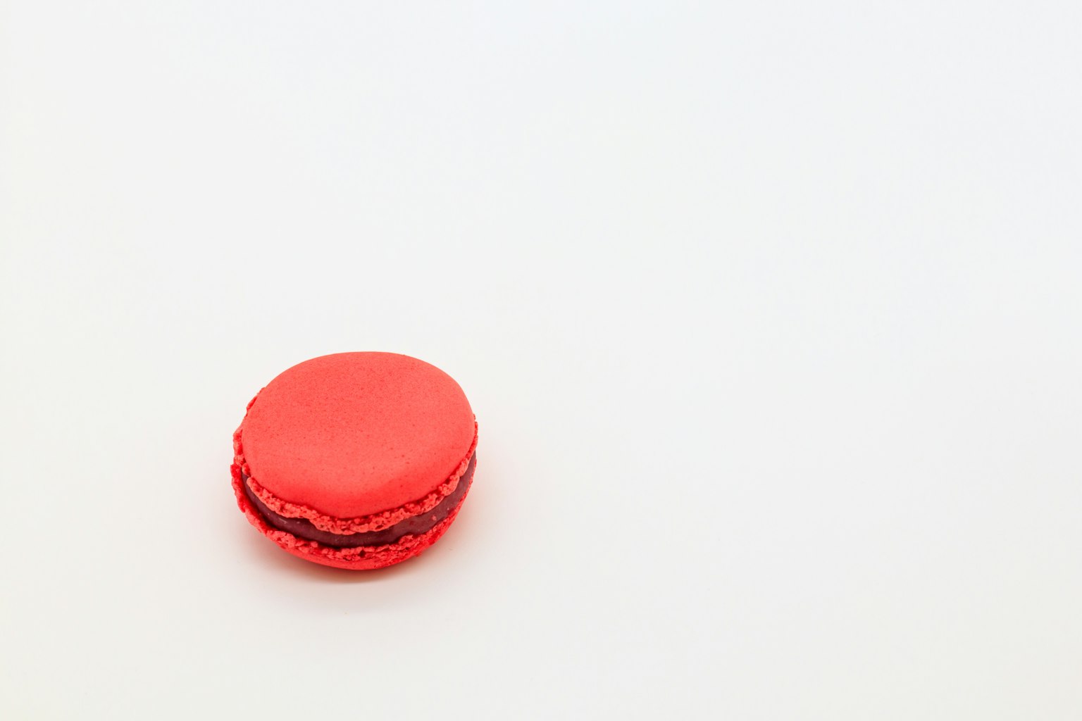 Un macaron rosso brillante posato su uno sfondo bianco