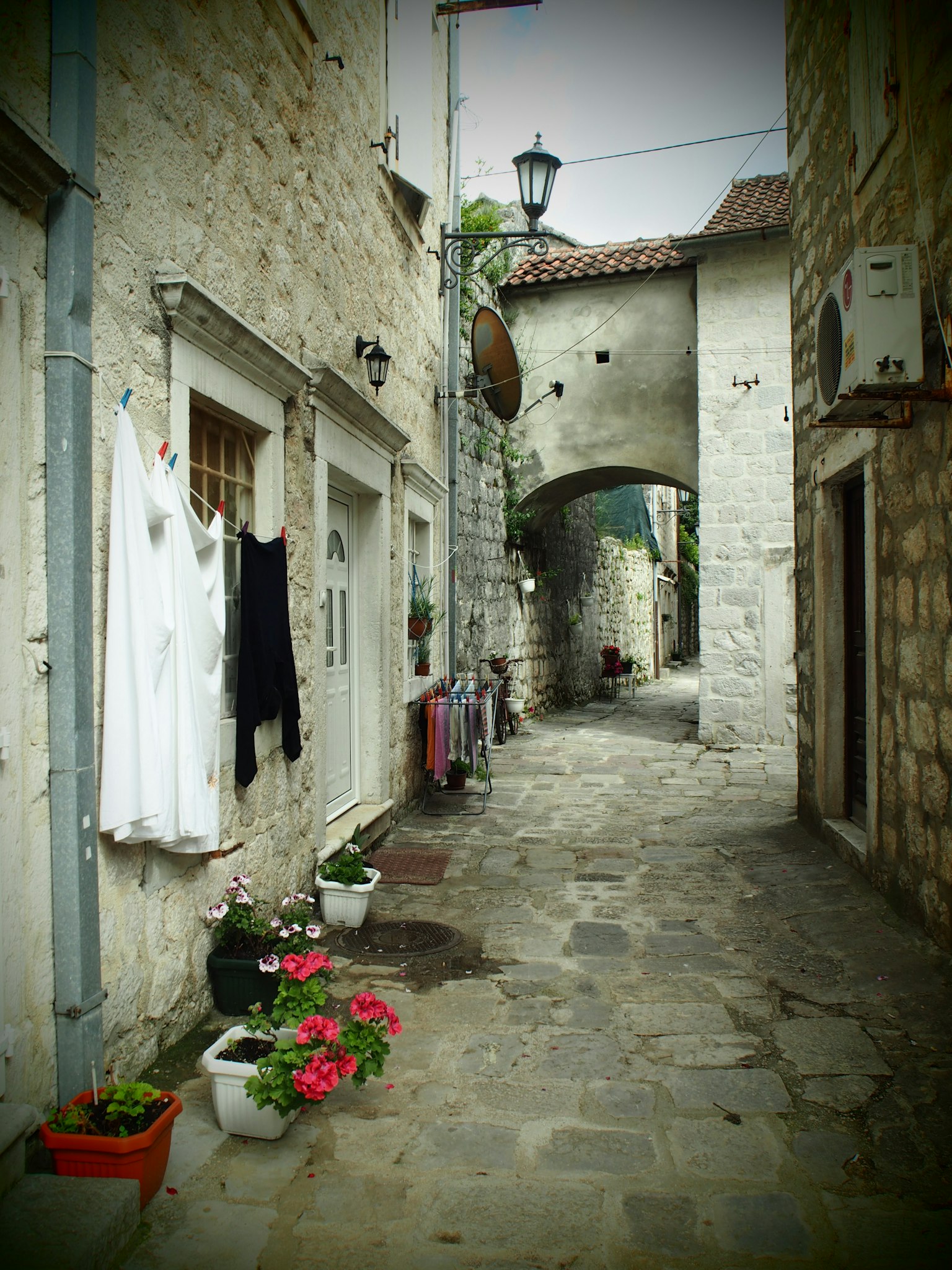 Callejón estrecho de piedra con ropa blanca colgando y macetas de flores