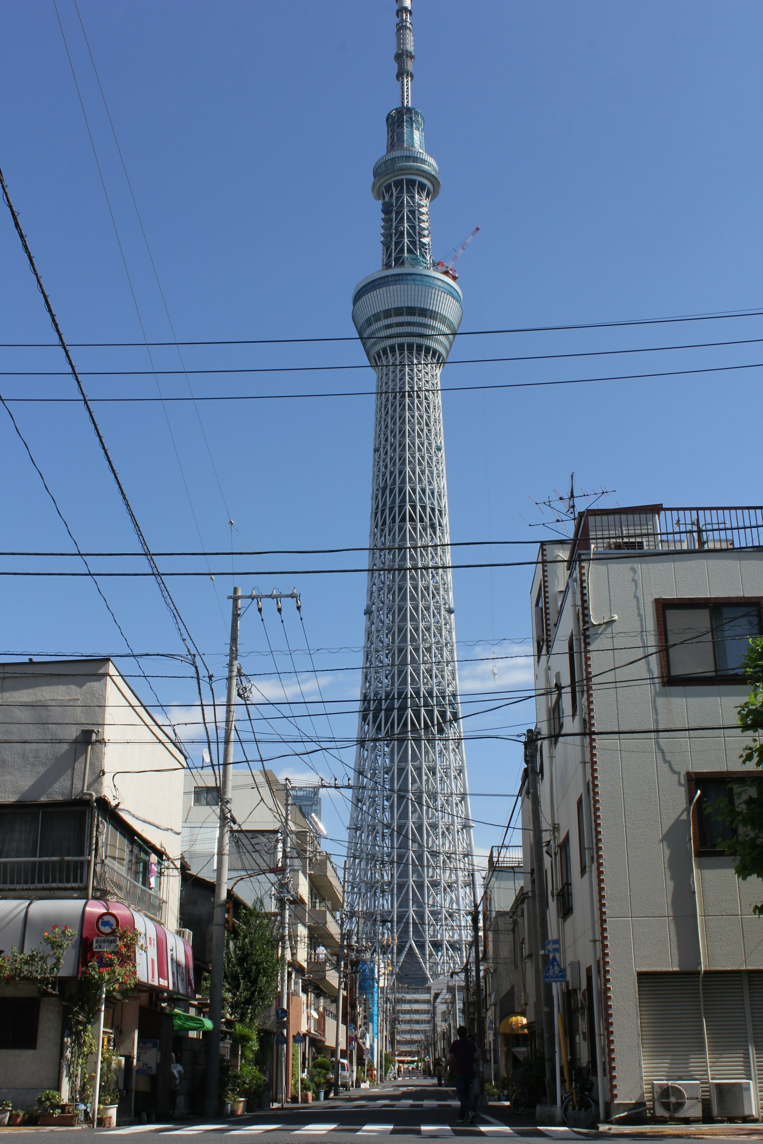 Tokyo Skytree che svetta su una strada cittadina sotto un cielo blu chiaro