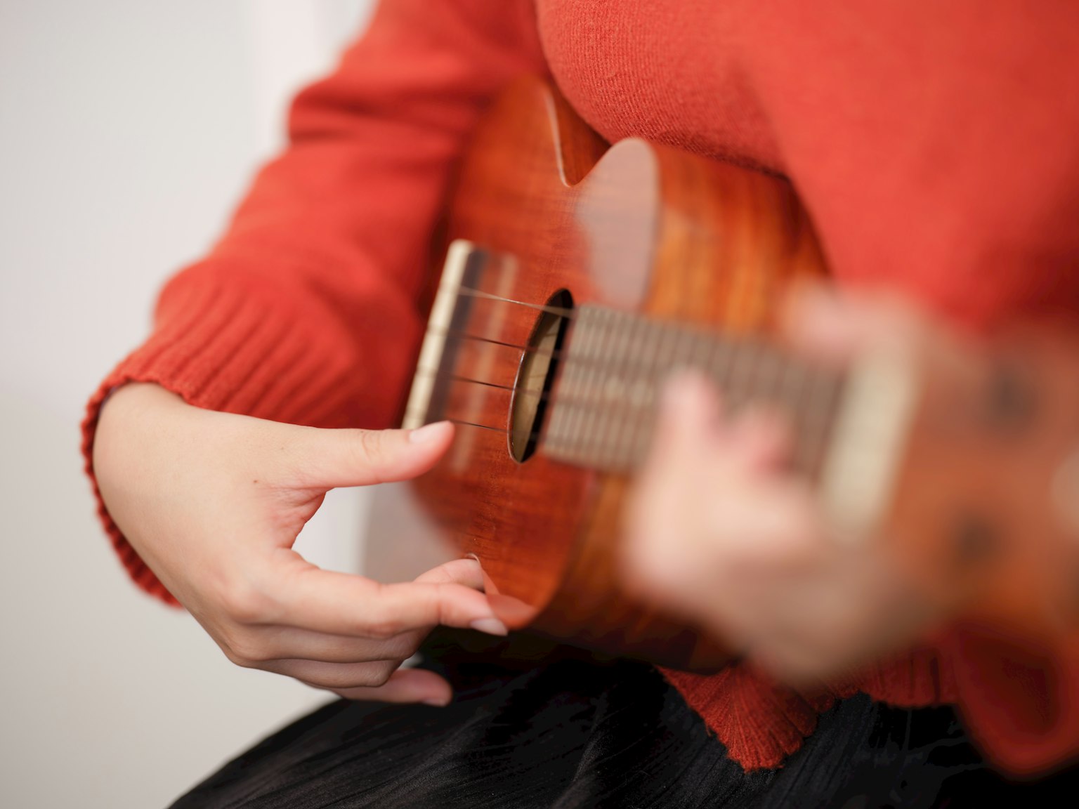 Close-up tangan bermain ukulele mengenakan sweater merah