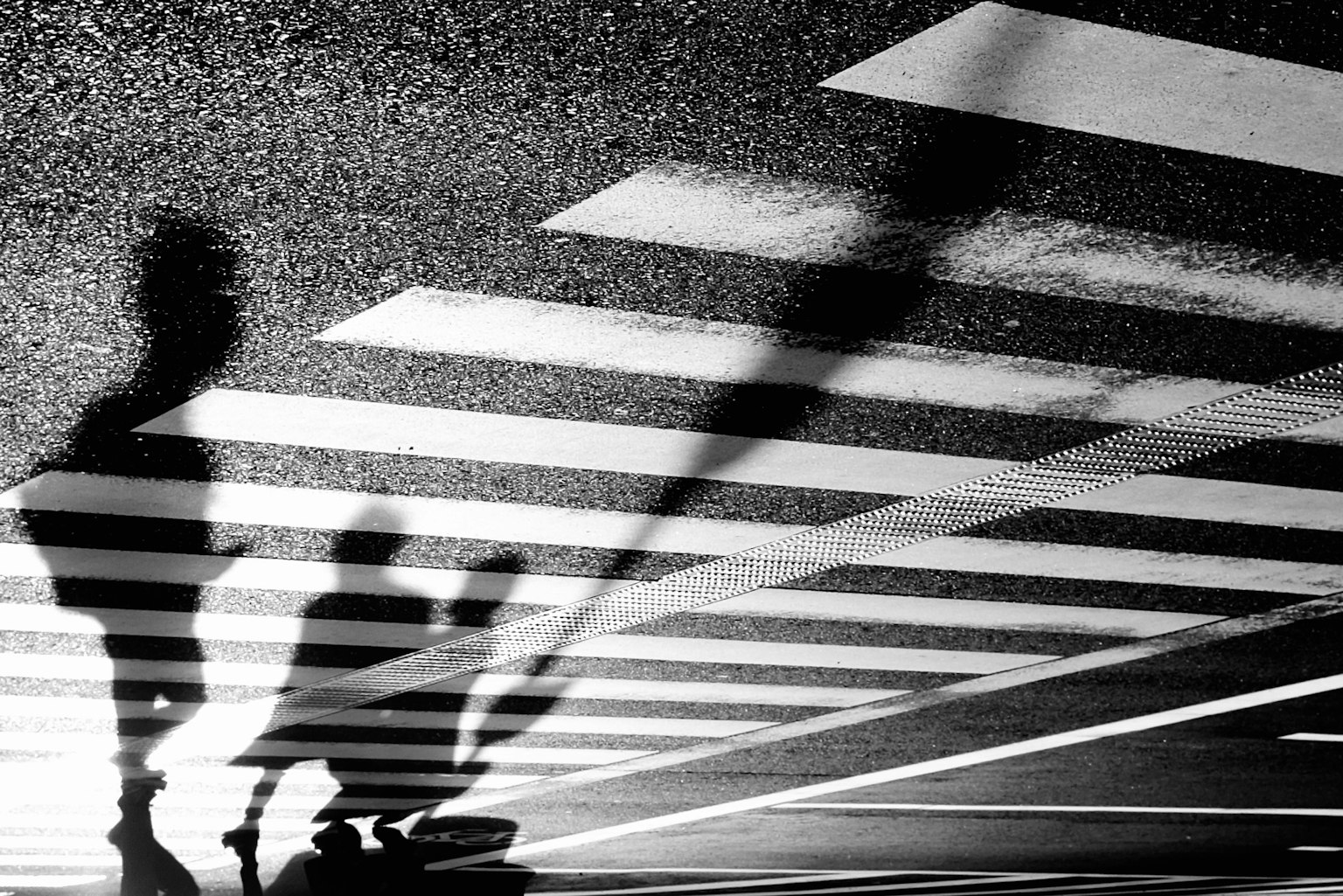 Shadows of people standing on a black and white crosswalk
