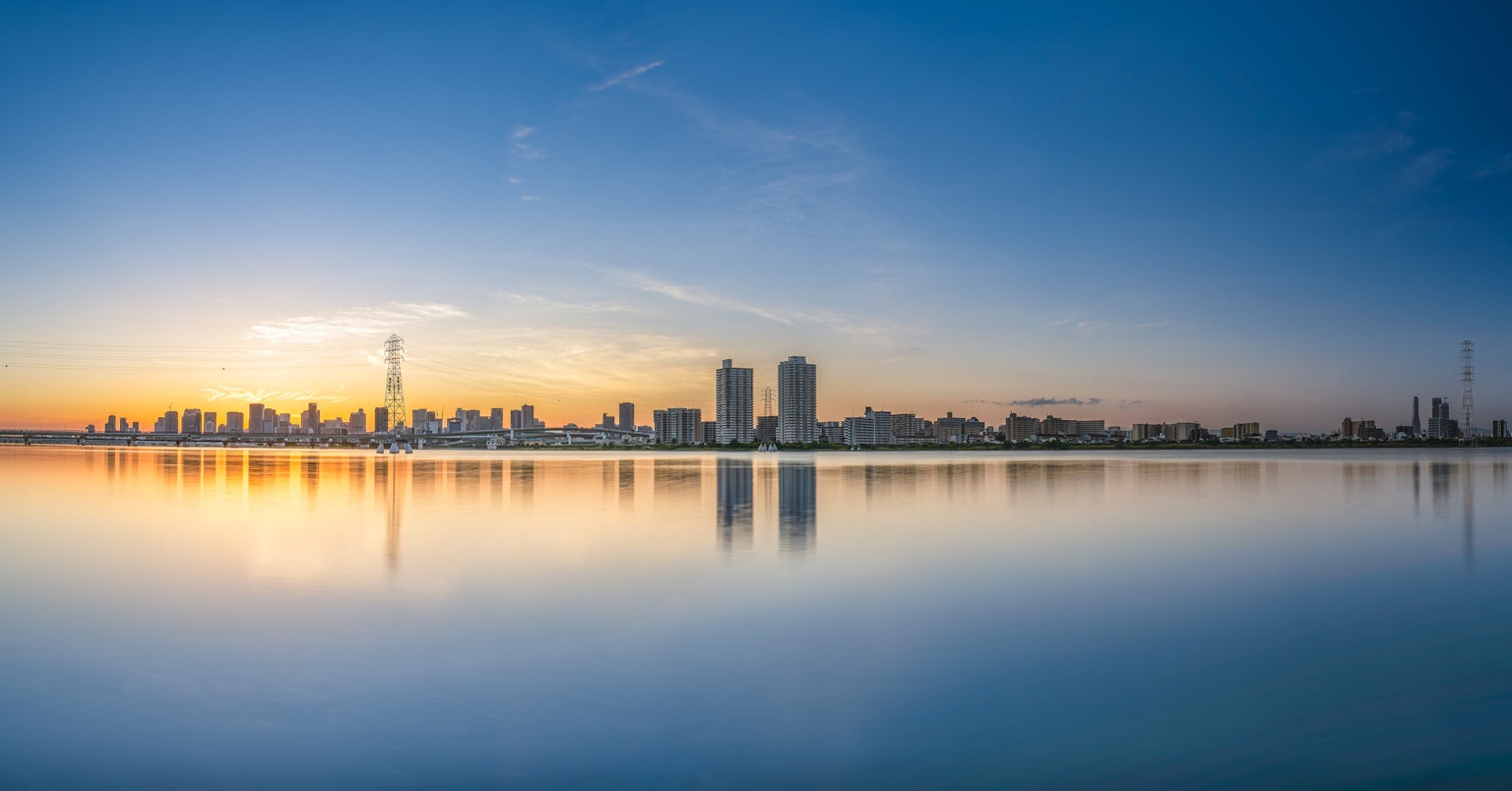 Vue panoramique d'une ligne d'horizon de ville au coucher du soleil avec des gratte-ciel se reflétant sur l'eau