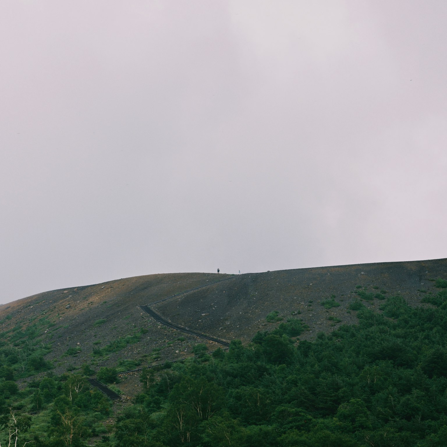Une petite silhouette debout au sommet d'une montagne sous un ciel nuageux