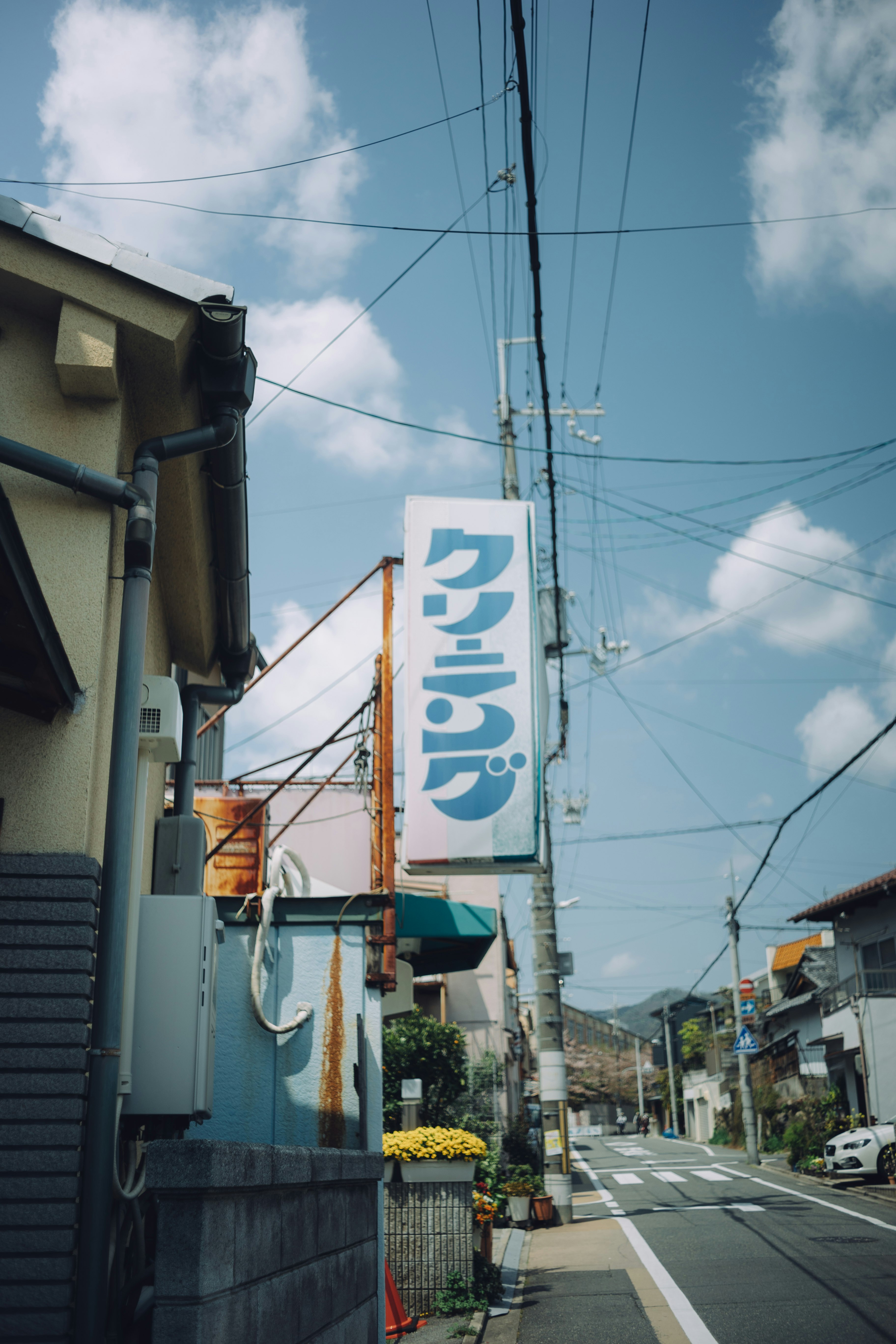 青空の下の電線と商店街の通りに立つ看板