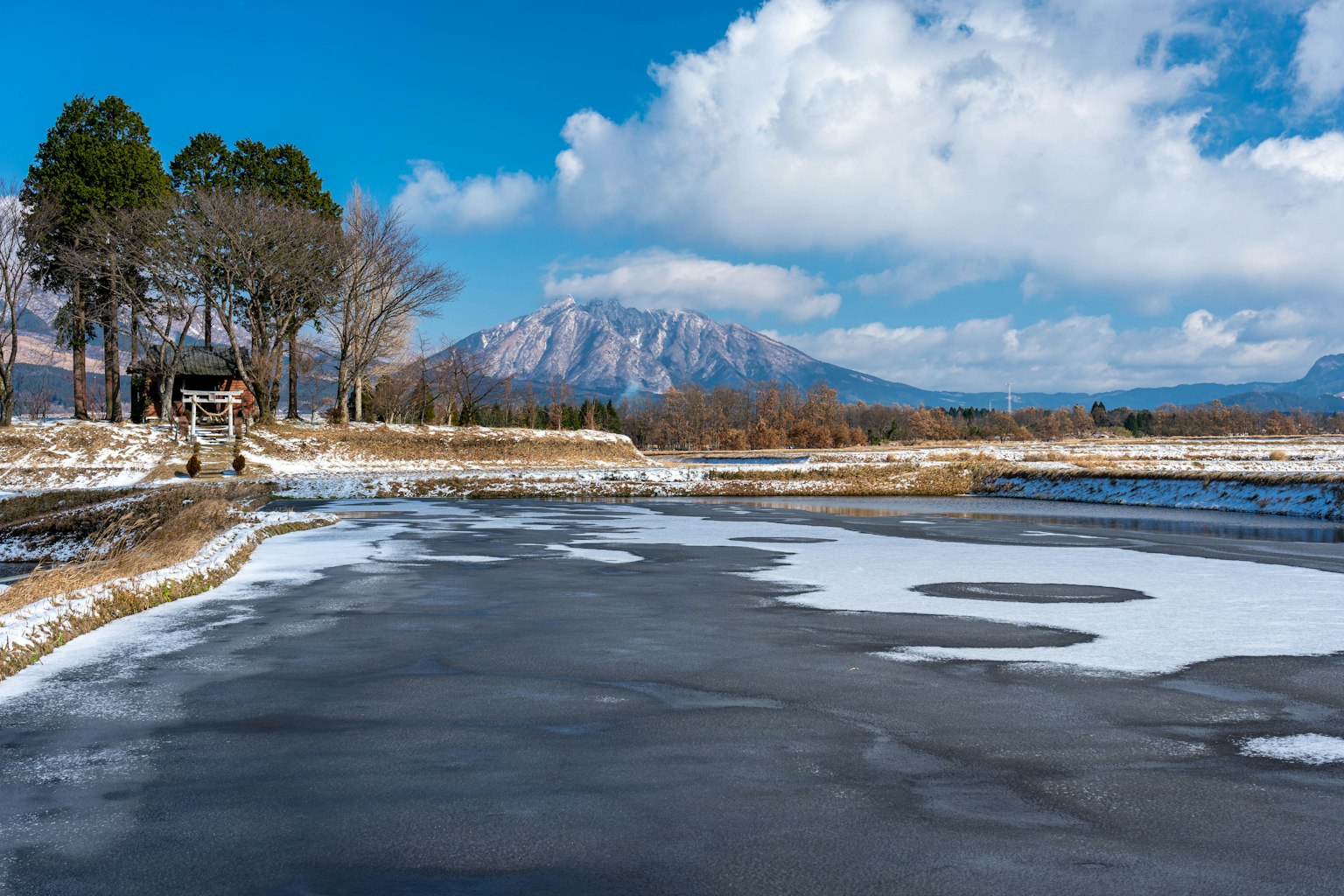Snowy lake landscape with mountains under a blue sky and white clouds