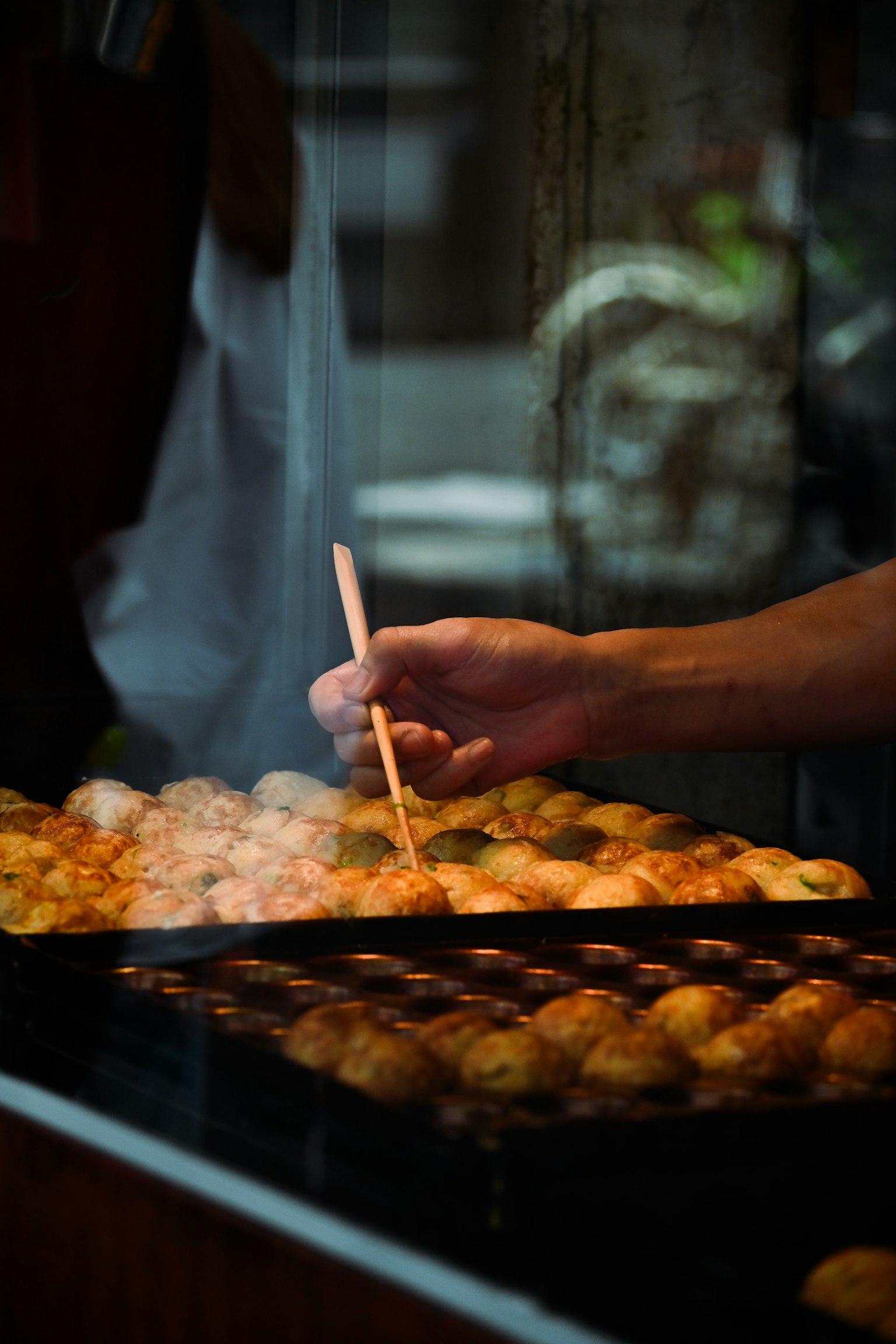 Kedekatan tangan yang memasak bola takoyaki yang hangat