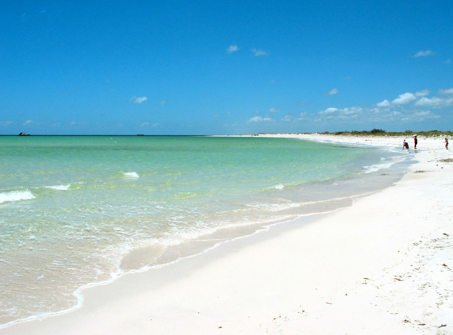 Malersicher Strandblick mit türkisfarbenem Wasser und weißem Sand unter einem klaren blauen Himmel