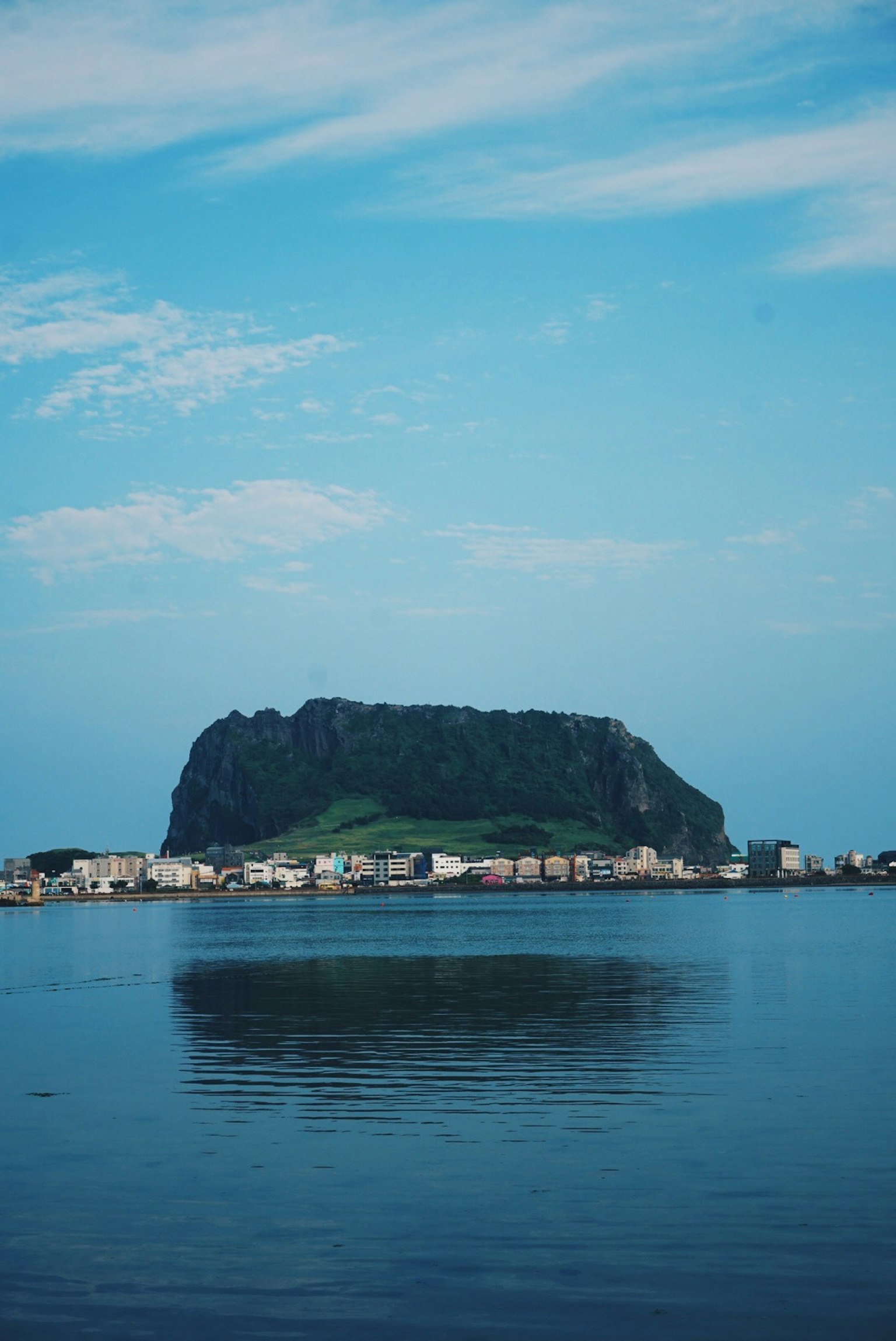 View of a mountain and village across calm water under a blue sky