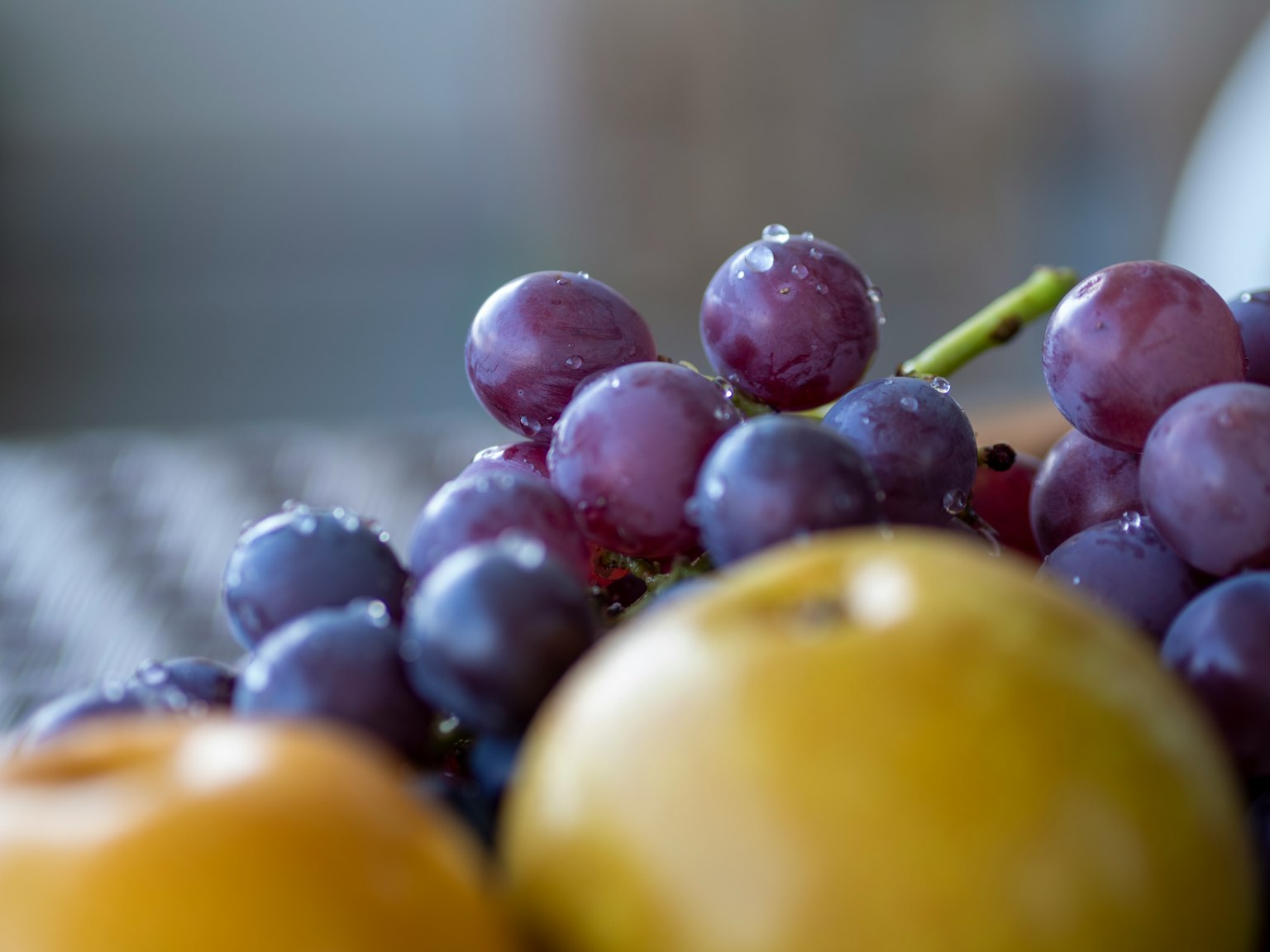 Nahaufnahme von lila Trauben mit Wassertropfen und einem gelben Apfel