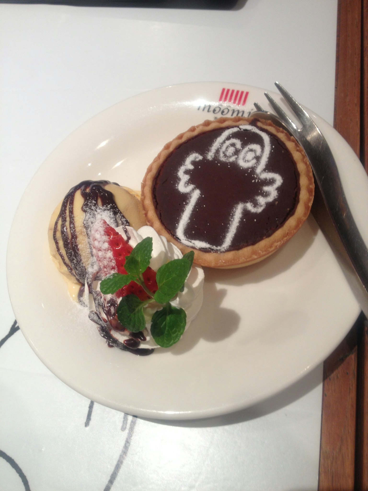 Bánh tart sô cô la với thiết kế nhân vật dễ thương và món tráng miệng kem tươi trên đĩa