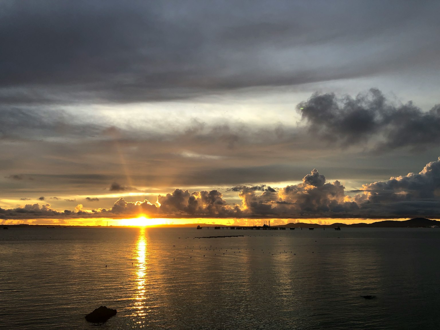 Sonnenuntergang über dem Ozean mit grauen Wolken und orangefarbenem Licht, das sich im Wasser spiegelt