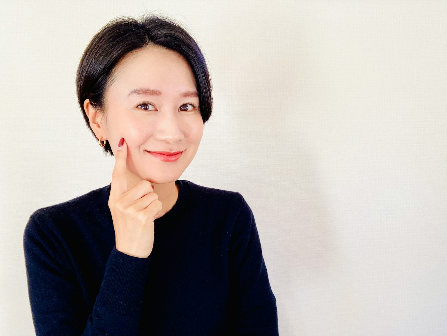一位穿著黑色毛衣的女性微笑著觸摸她的臉頰
