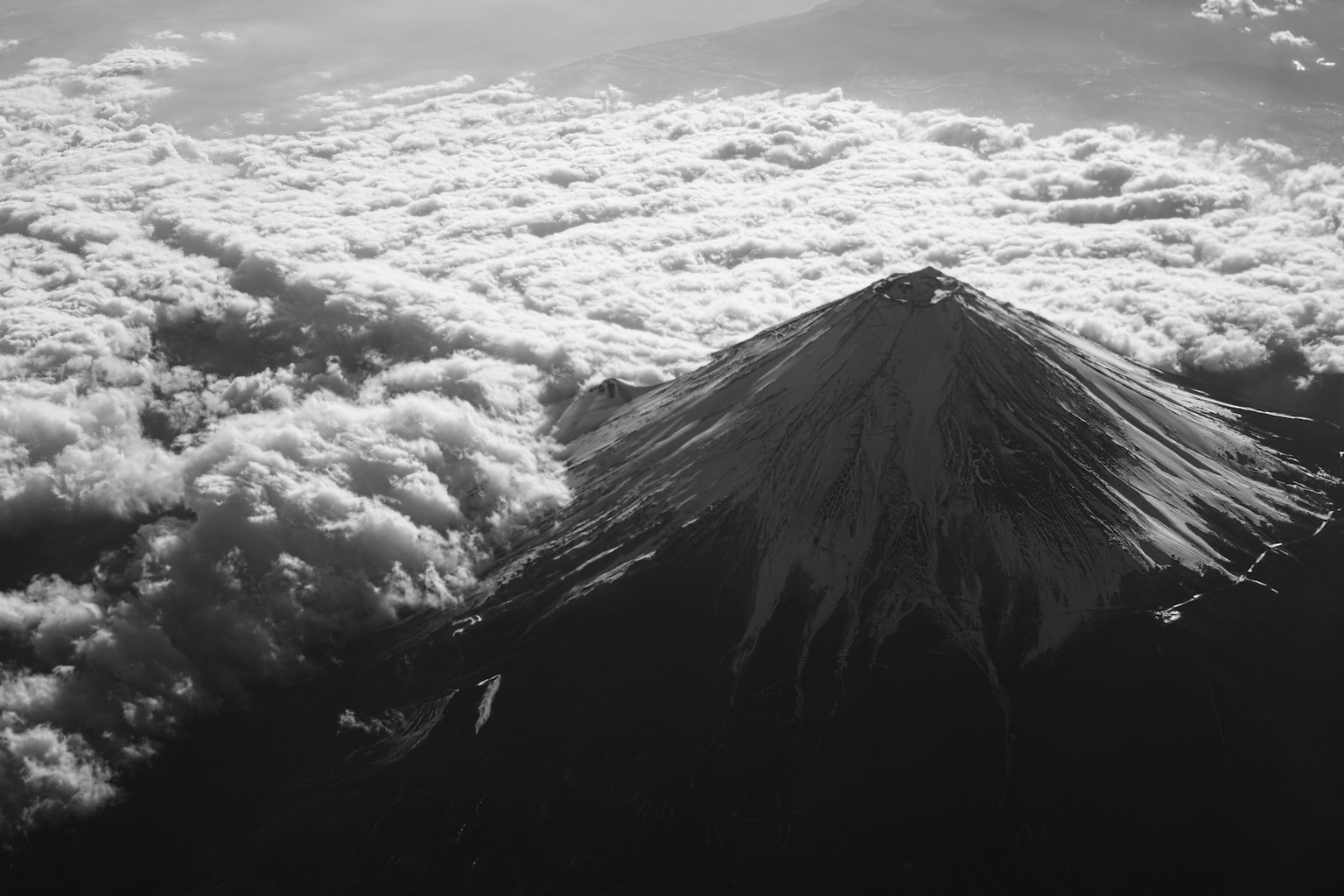 Luftaufnahme des Fuji, der über einem Wolkenmeer in Schwarzweiß auftaucht
