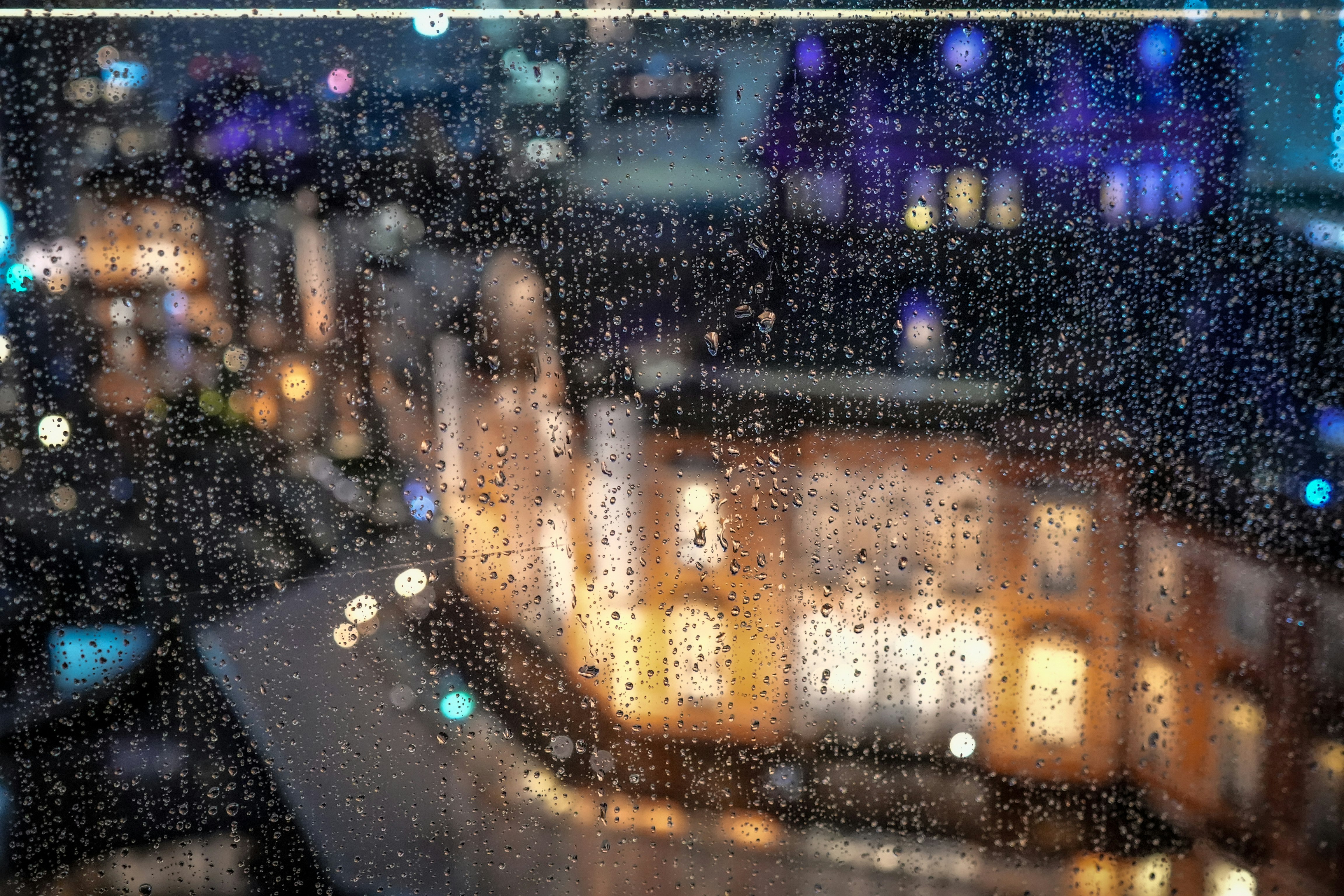 雨粒の降る窓越しに街の光がにじむ夜景