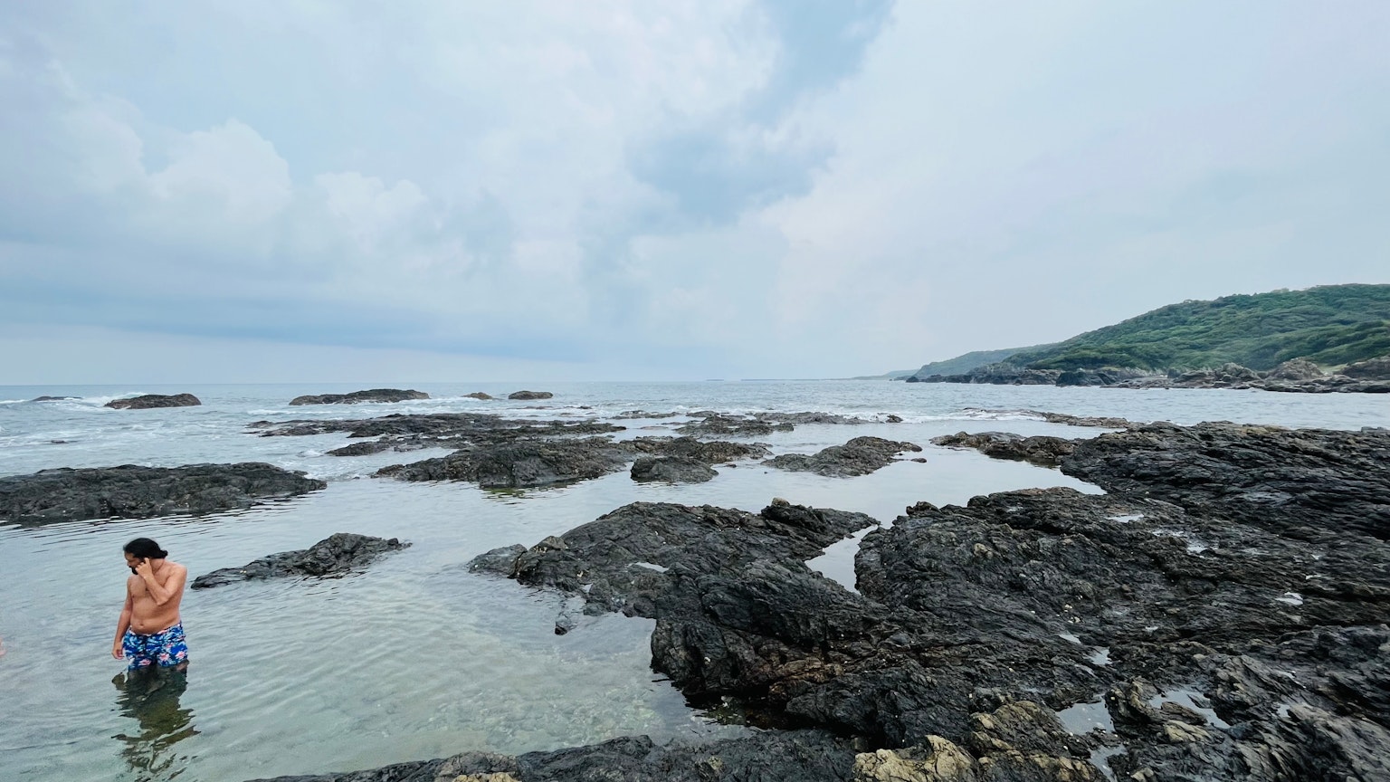 孩子在岩石海岸玩耍，海面平静，天空多云