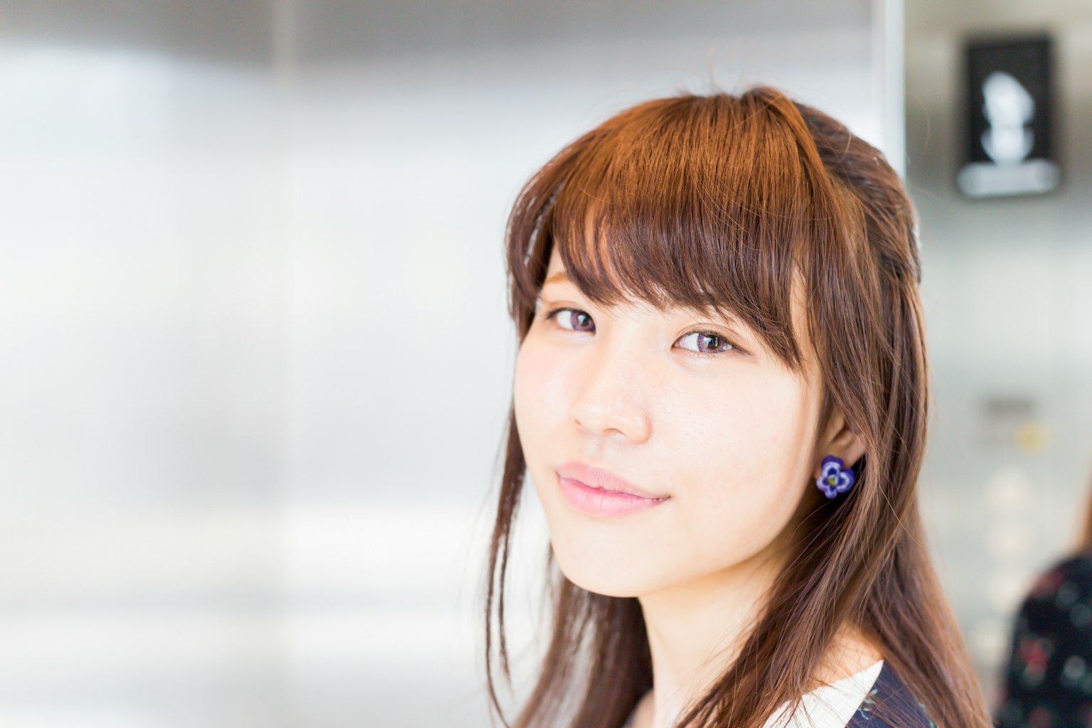 Portrait of a young woman with long brown hair wearing blue earrings blurred metallic background