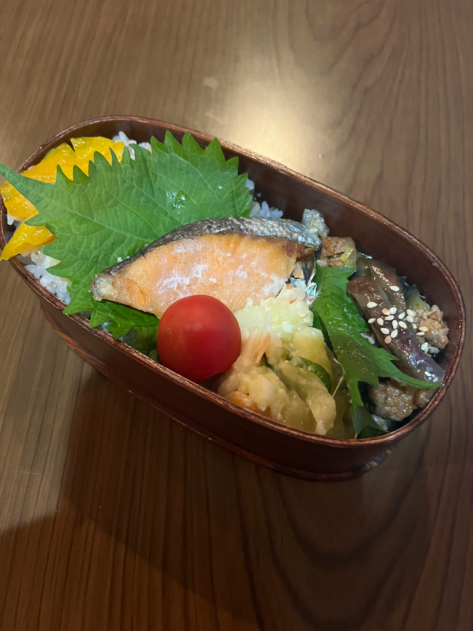 便當盒的圖片包含鮭魚片米飯綠葉和櫻桃番茄