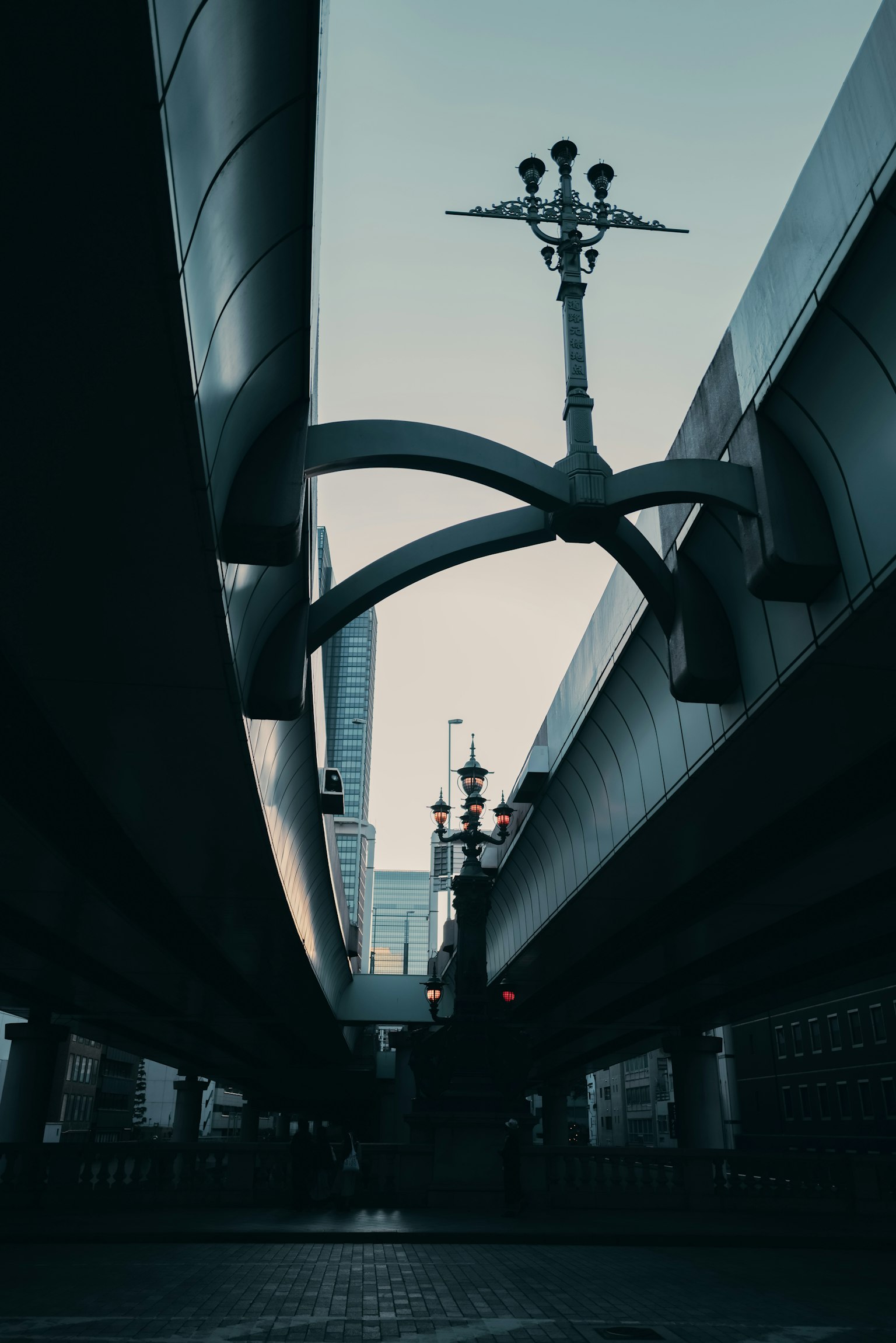 Photo of a structure viewed from underneath an overpass featuring steel beams and streetlights