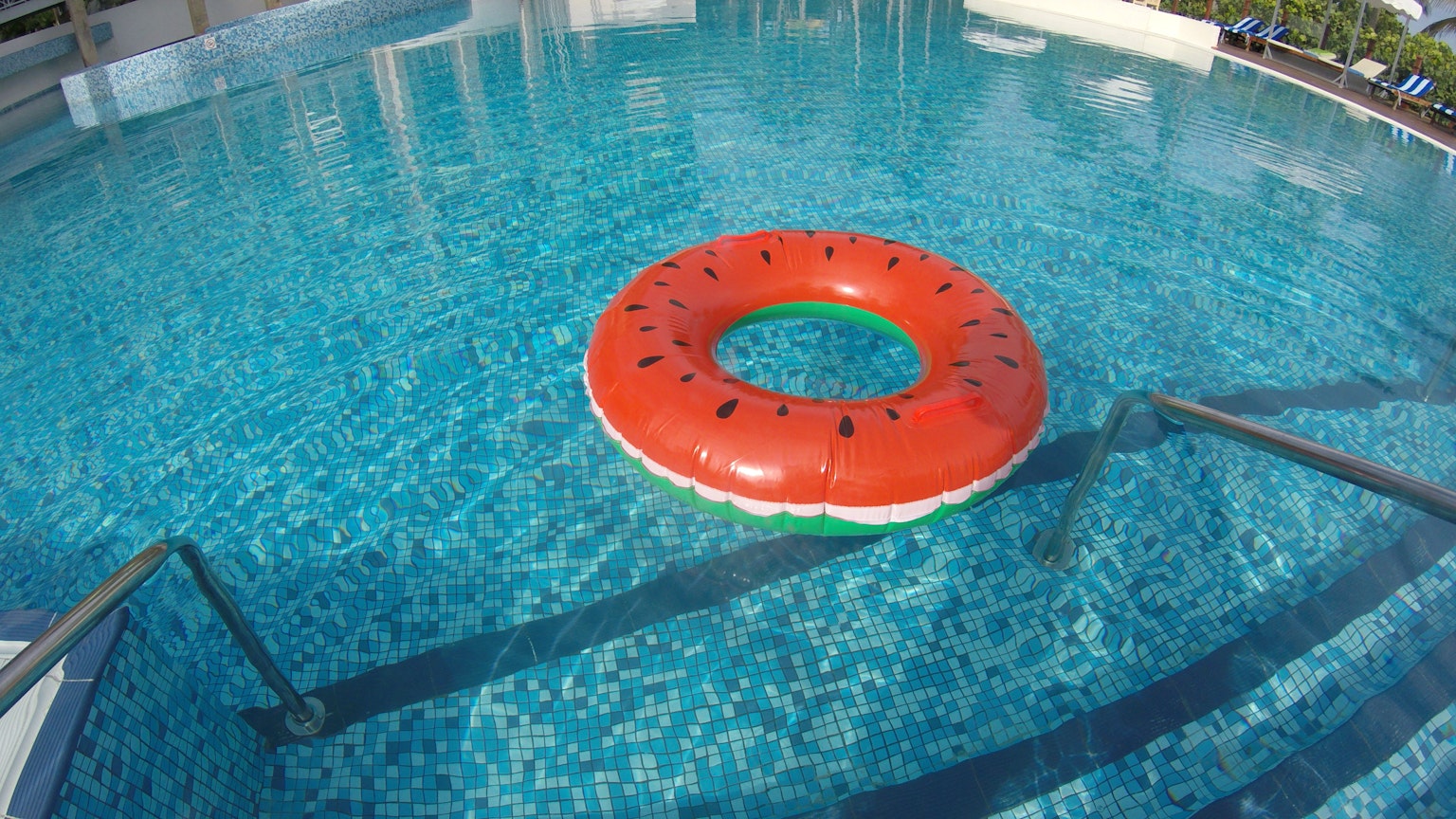 Watermelon-shaped float in a swimming pool with blue tiles