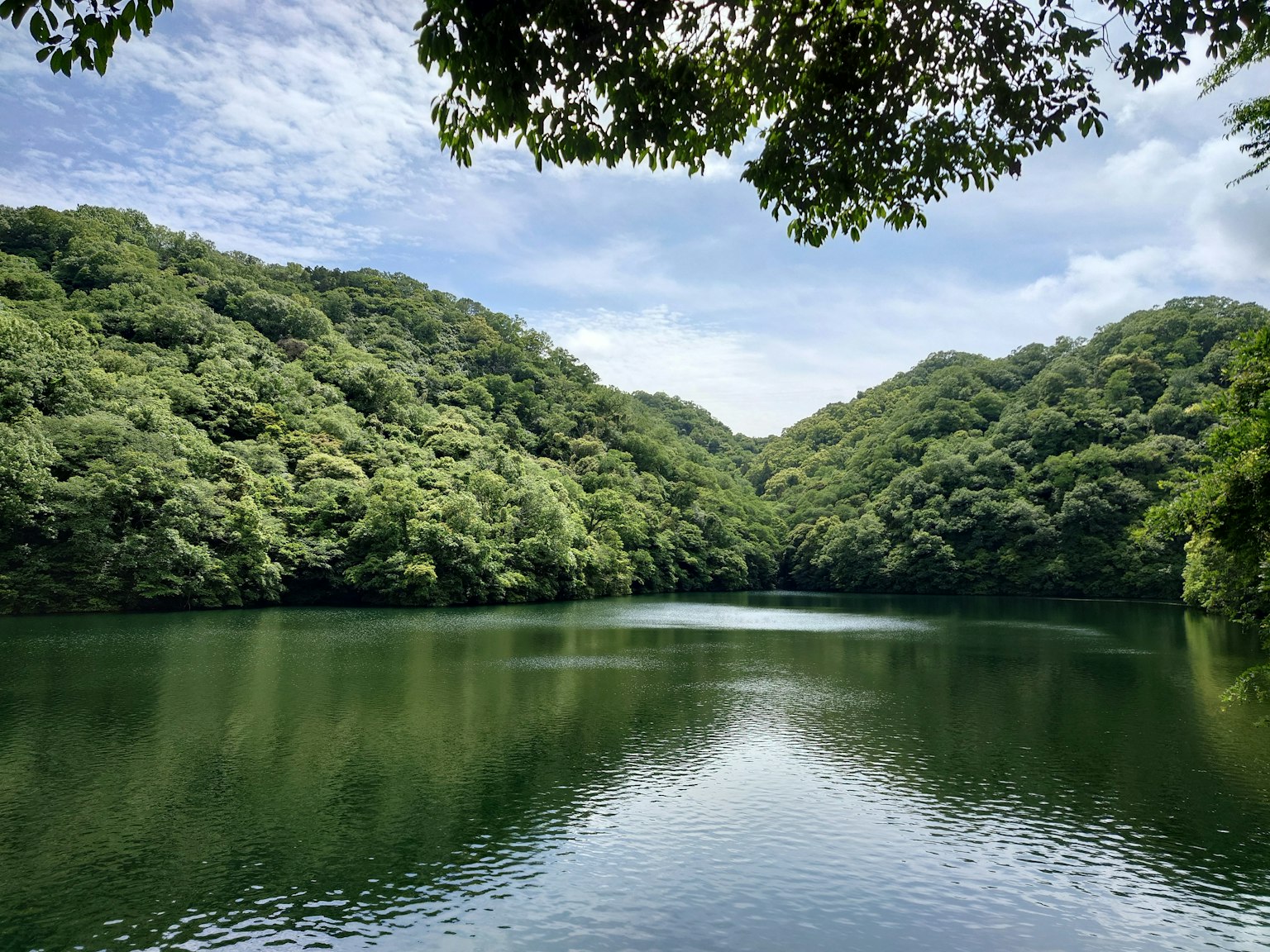 Lago sereno rodeado de colinas verdes bajo un cielo parcialmente nublado