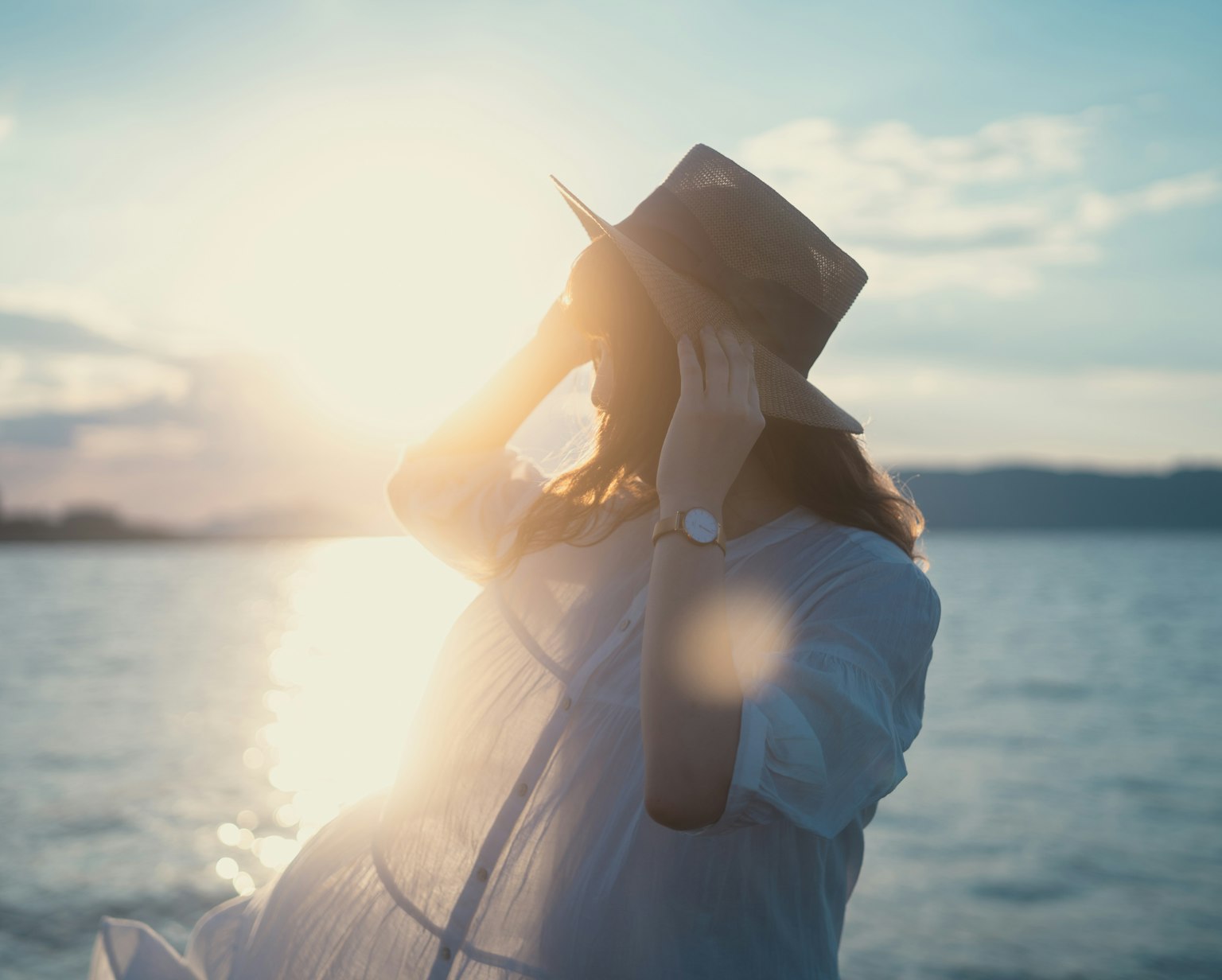 海邊一位戴著帽子的女性剪影在陽光下享受