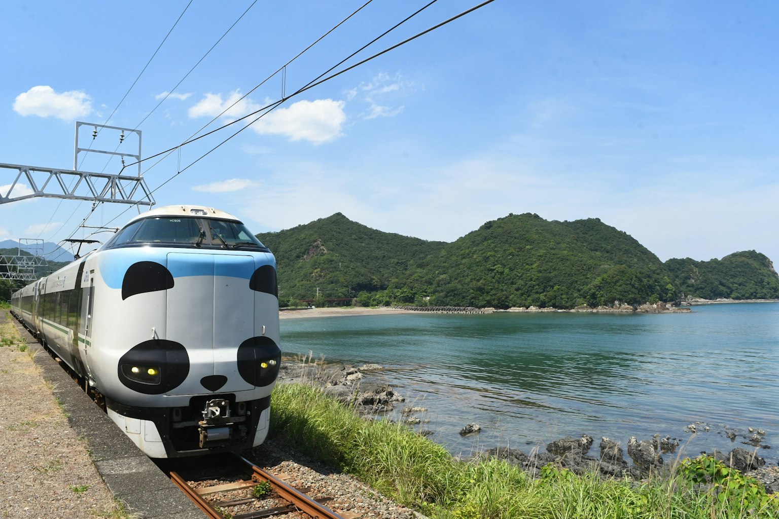 Un train distinctif garé près de la mer avec un ciel bleu et des montagnes en arrière-plan